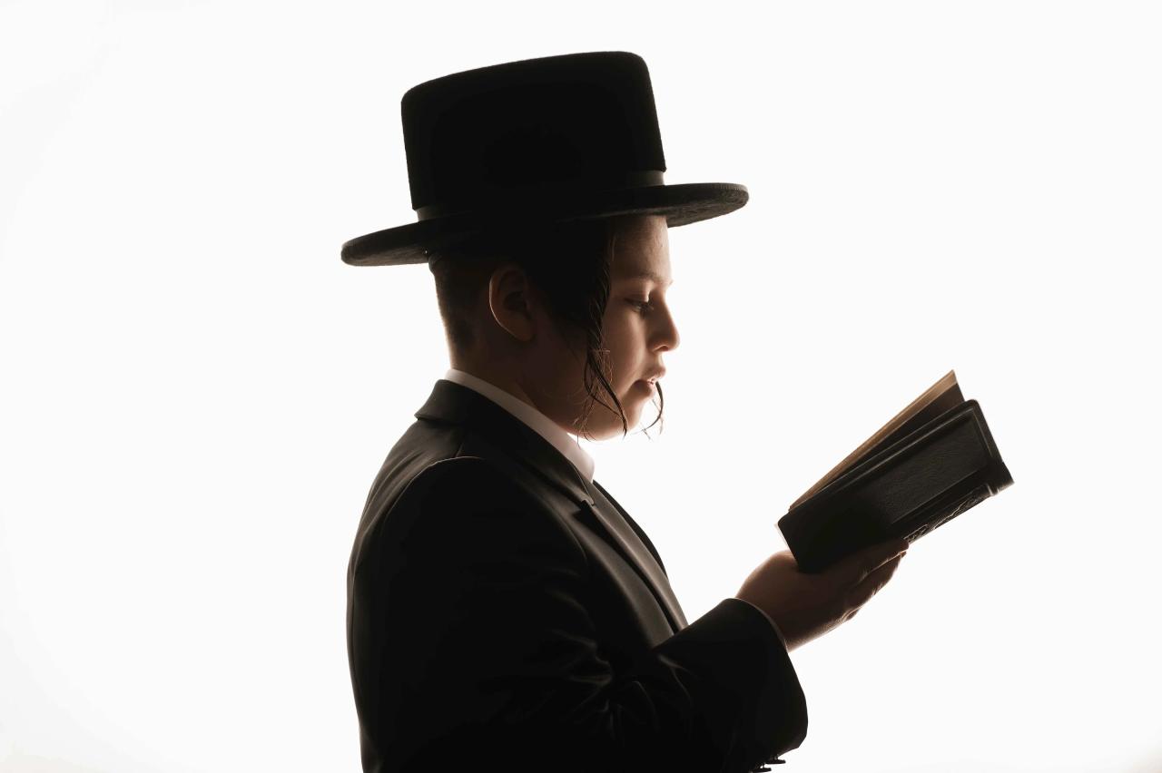 Man wearing a black hat reading from a book in a bright, minimal background silhouette.