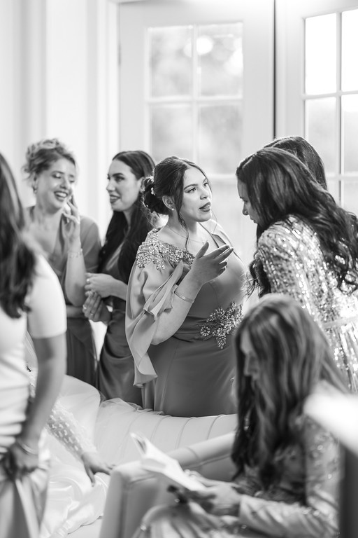Black-and-white photo of the bride and friends seated indoors, smiling and watching an event off to the right.