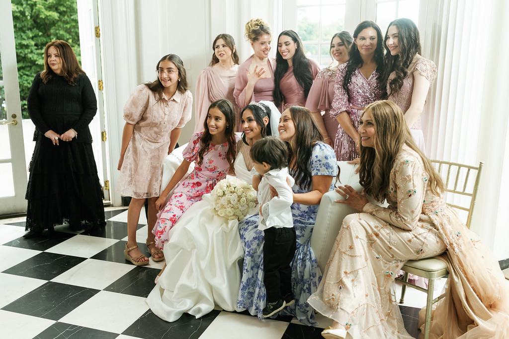 Group of women and children seated together indoors during a family moment, smiling toward the camera with a bouquet at the center.