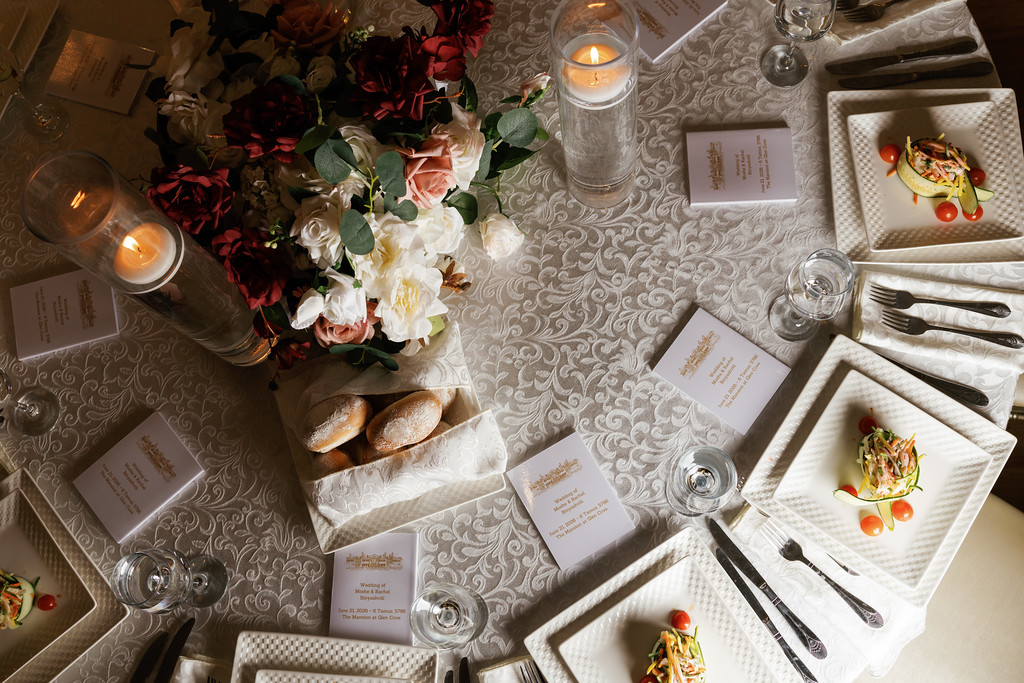 Top-down view of a decorated wedding reception table with candles, floral centerpiece, and plated place settings with menu cards.