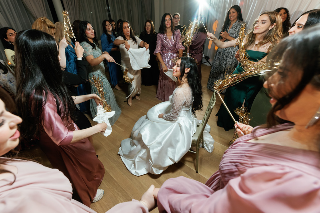 The bride seated on the dance floor in a white gown is surrounded by guests holding sparklers and celebrating at a wedding reception.