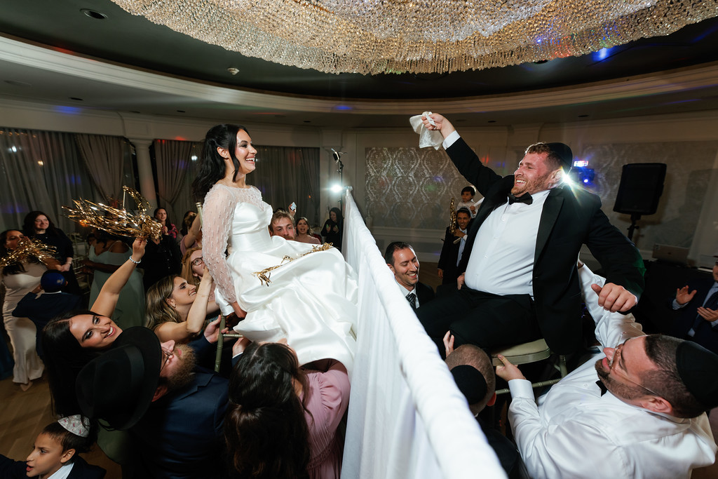 Frum wedding couple dancing and celebrating with joyful laughter, surrounded by family at the reception.