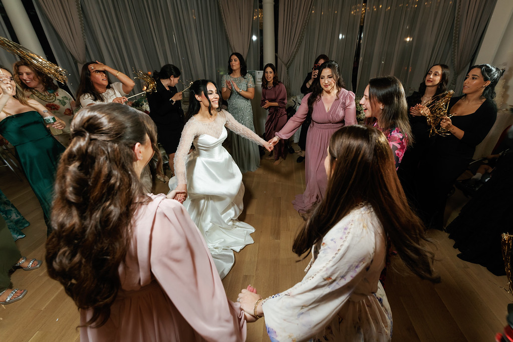 Bride in a white gown dancing in the center while guests in dresses and formalwear circle around her during the wedding reception.