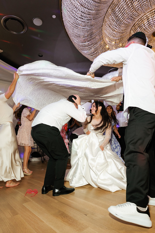 Bride and groom dancing at a frum wedding under a decorated canopy, surrounded by smiling guests in the reception hall.