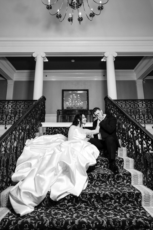 Black-and-white photo of a bride in a flowing white veil and dress embracing her groom while they stand on a staircase during the badeken moment.