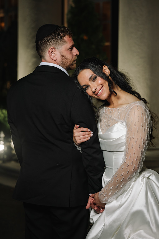 A bride and groom embrace during their wedding at night, smiling as they hold each other closely.