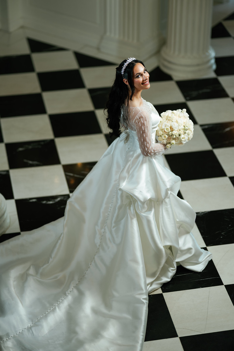 Bride in a white gown holding a bouquet, smiling as she turns in an at The Mansion At Glen Cove, photographed by CJ Studios