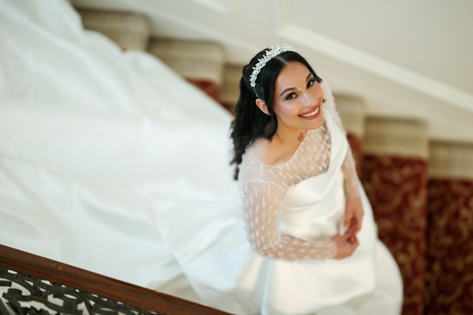 Frum wedding bride smiling on a staircase in a white lace dress with at The Mansion At Glen Cove, photographed by CJ Studios