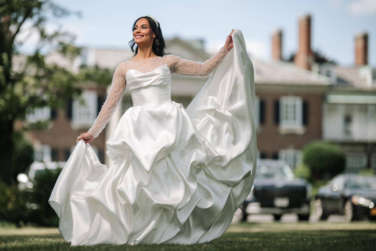 Woman in a white wedding gown smiling while lifting her veil during at The Mansion At Glen Cove, photographed by CJ Studios. Wedding photography.