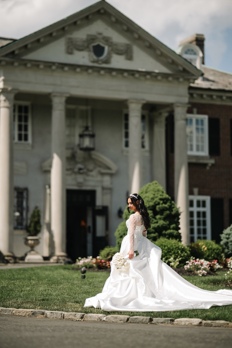 Bride in a white wedding gown and veil posing on a garden lawn at The Mansion At Glen Cove, photographed by CJ Studios