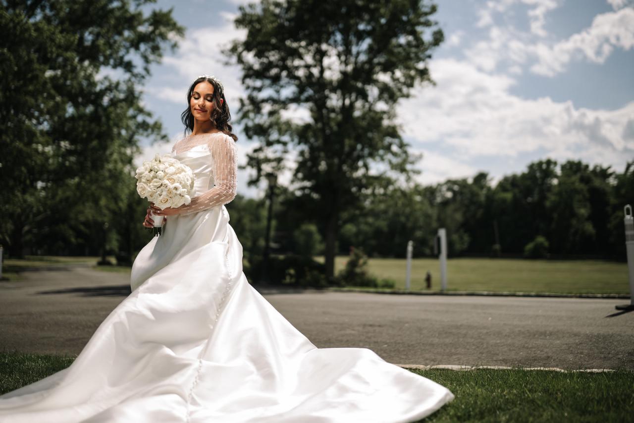 Bride holding a white floral bouquet outdoors, wearing a long sleeve at The Mansion At Glen Cove, photographed by CJ Studios. Wedding photography.