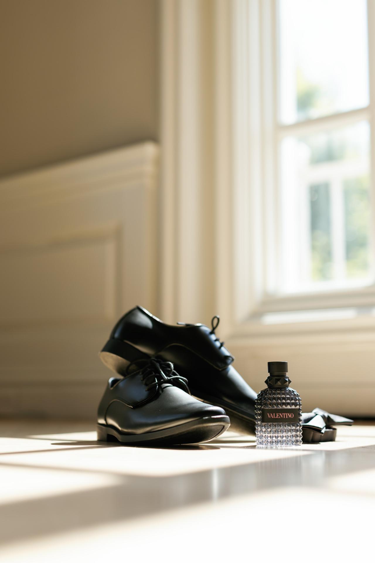 Black dress shoe and a Valentino cologne bottle arranged together on at The Mansion At Glen Cove, photographed by CJ Studios. Wedding photography.
