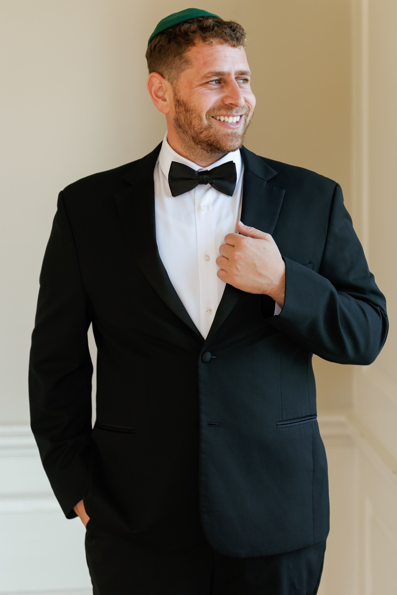 Black-and-white portrait of a groom in a tuxedo adjusting his bow at The Mansion At Glen Cove, photographed by CJ Studios
