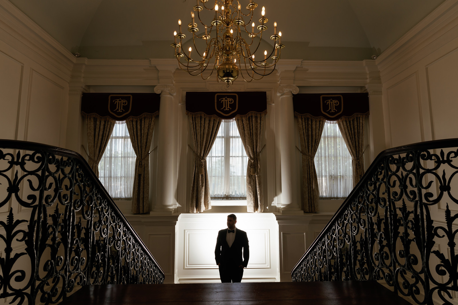 Silhouetted groom in a black suit and bow tie standing on a grand at The Mansion At Glen Cove, photographed by CJ Studios