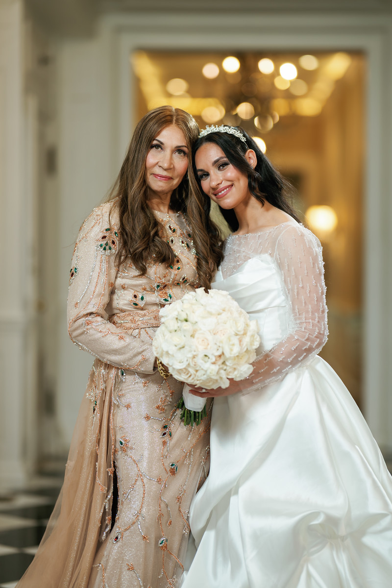 Smiling bride in a white gown holding a bouquet embraces an older at The Mansion At Glen Cove, photographed by CJ Studios