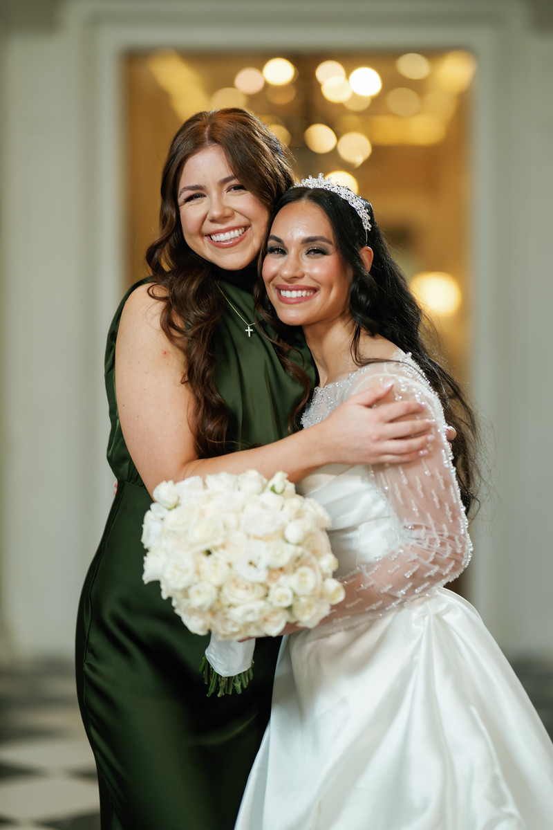 Two women smiling as they embrace during a wedding reception, with a at The Mansion At Glen Cove, photographed by CJ Studios