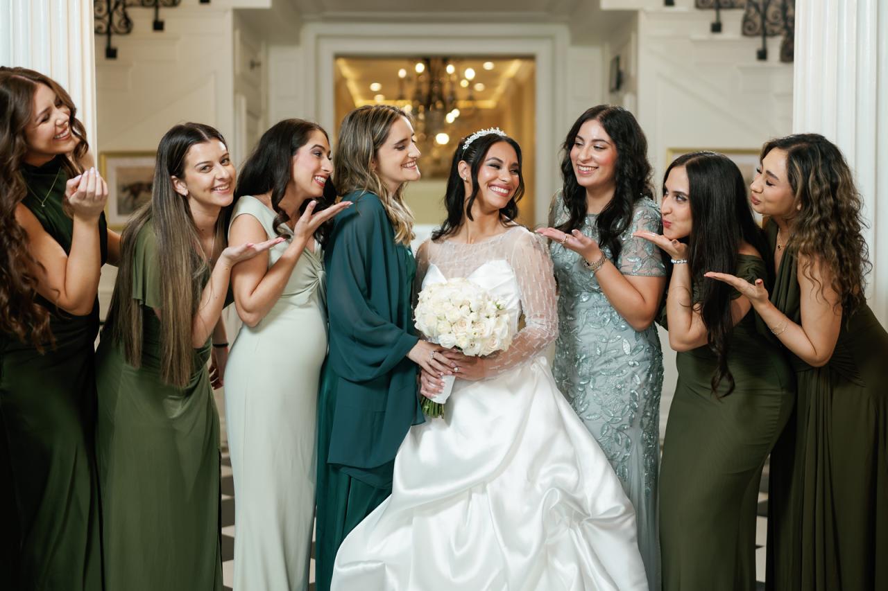 Bride smiling while her bridesmaids and friends in green dresses at The Mansion At Glen Cove, photographed by CJ Studios. Wedding photography.