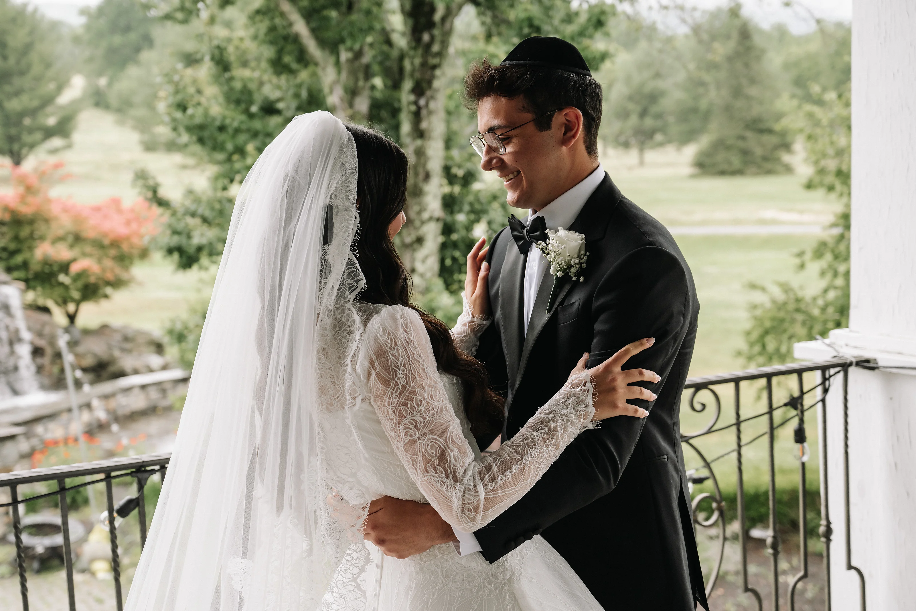 Bride and groom in an intimate embrace outdoors during the wedding, with the bride’s veil and lace sleeves and the groom’s joyful smile.