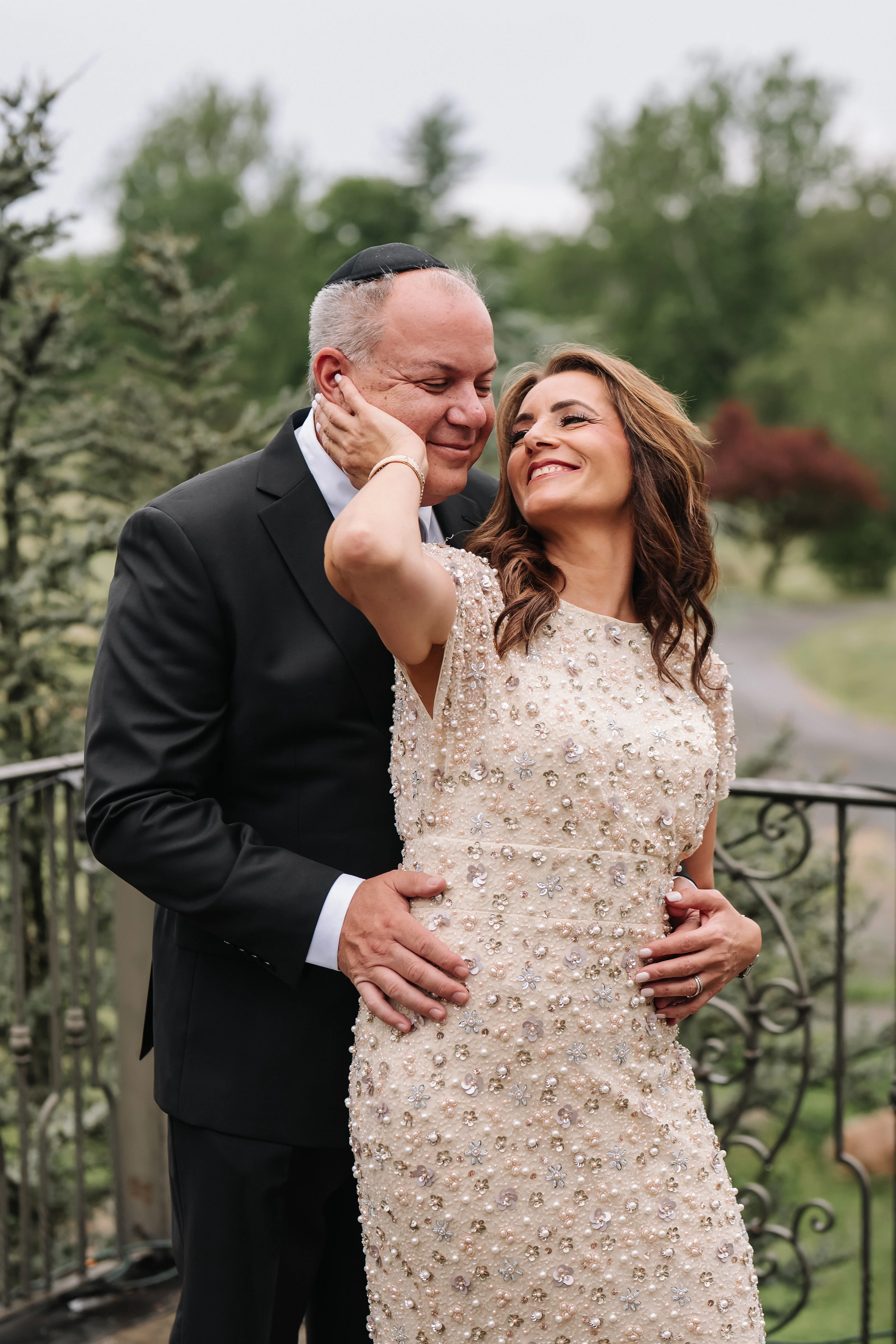 Bride and groom embracing outdoors, laughing together during wedding portraits with greenery in the background.