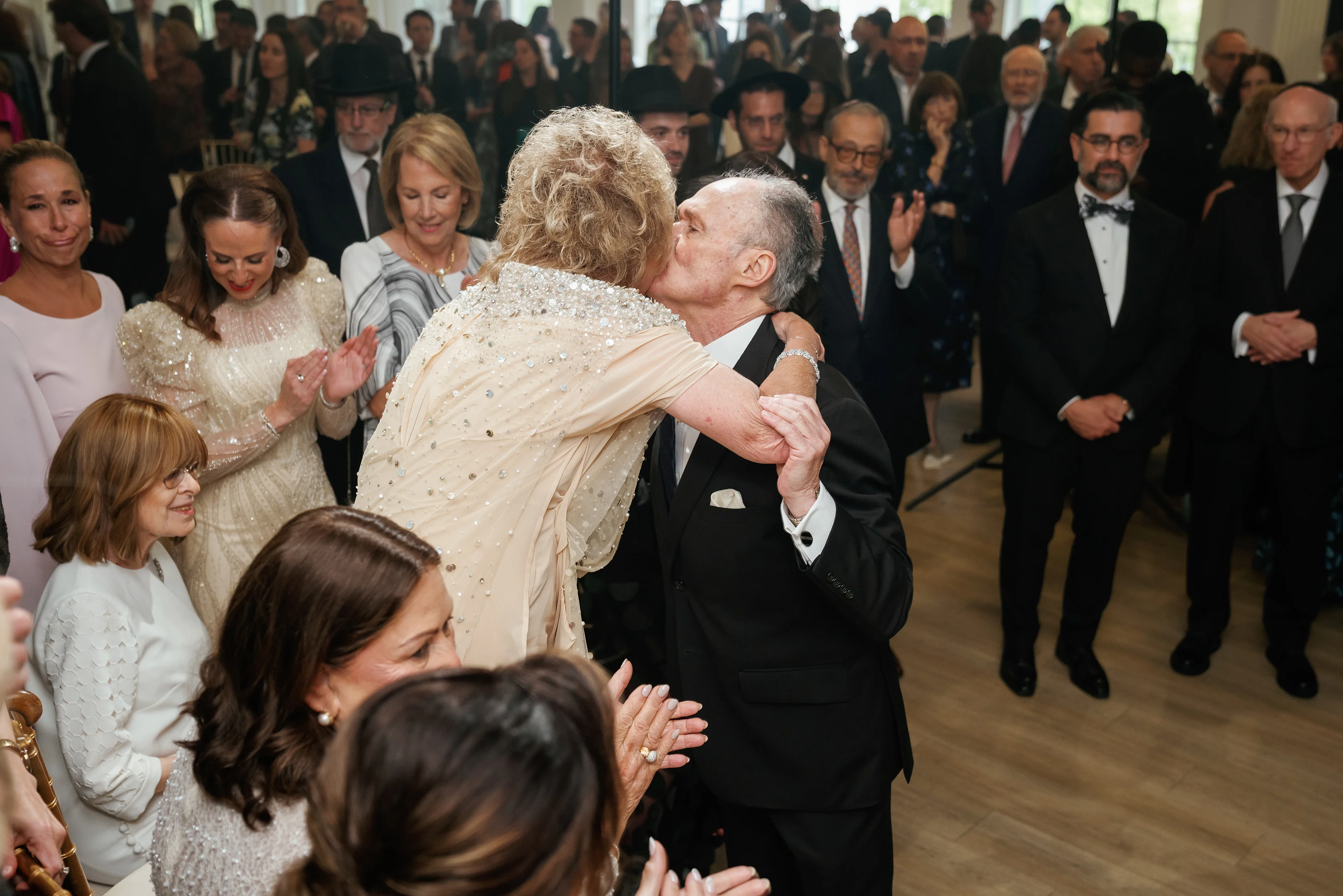 Bride and groom embracing in the middle of a wedding dance floor while guests watch in the background.