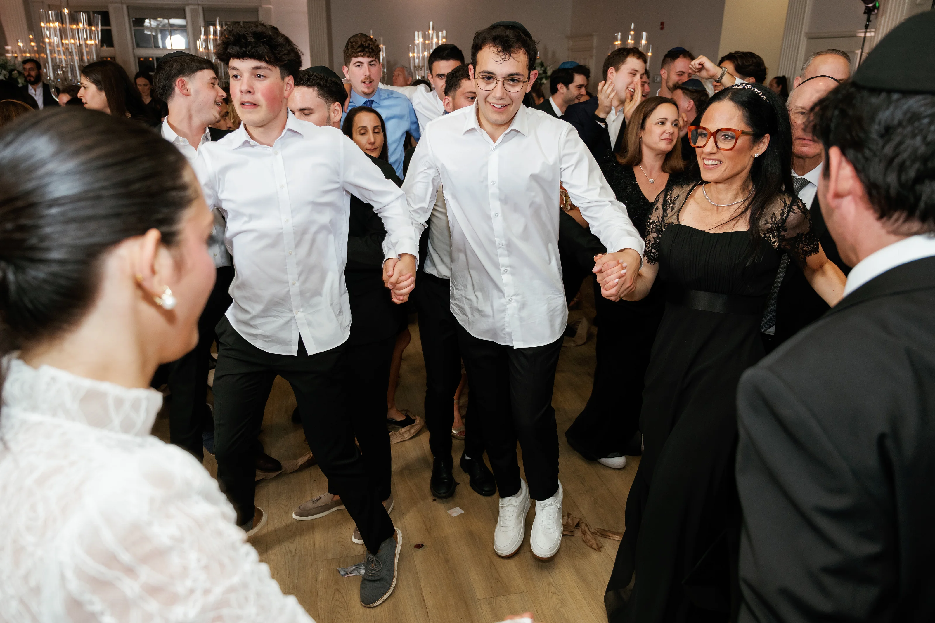 Candid dance-floor moment at a bar mitzvah with guests smiling and moving under warm indoor lighting.