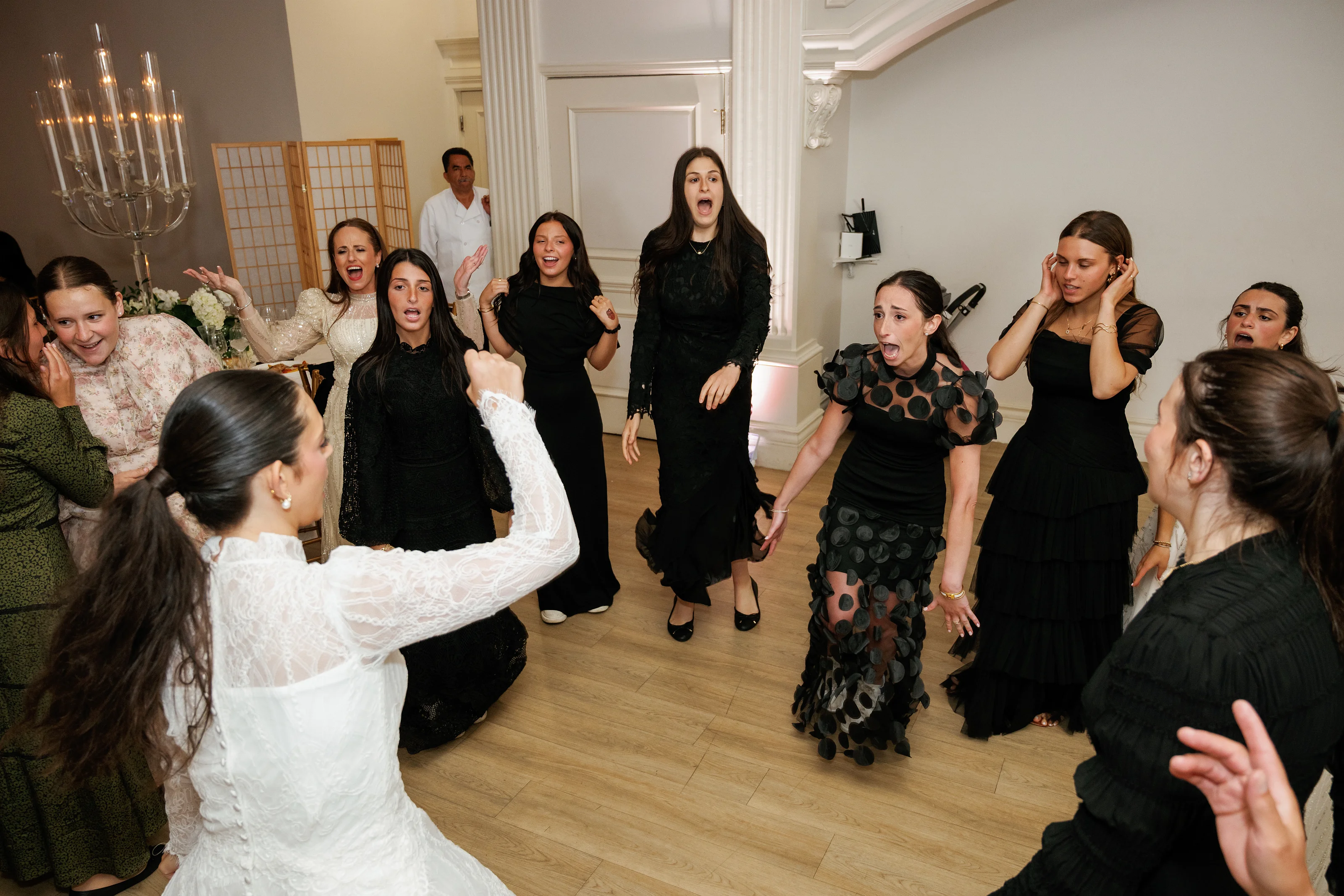 Group of wedding reception guests dancing and cheering with hands raised in a ballroom.