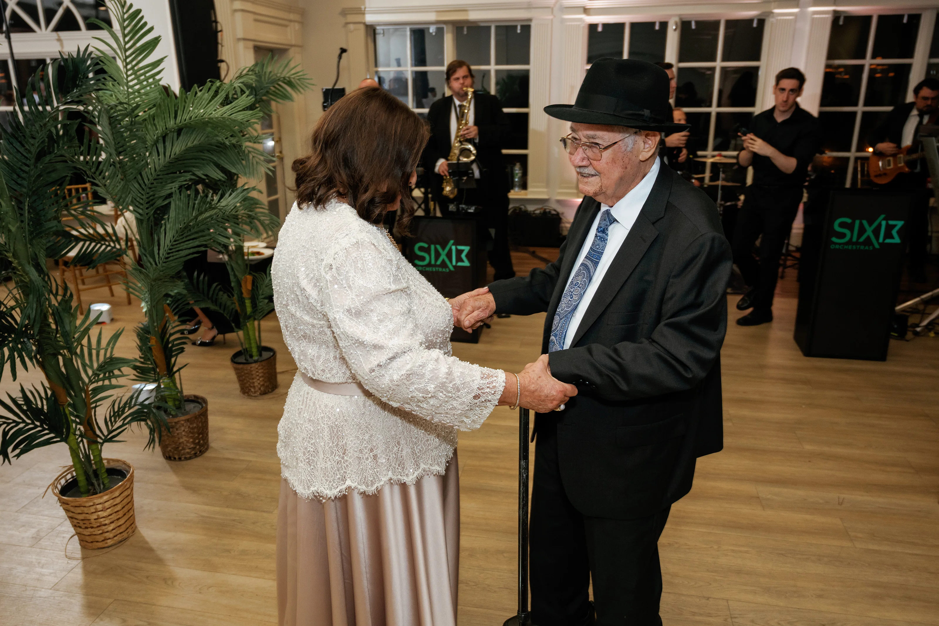 Bride holding hands with an elderly man during a celebration indoors with musicians in the background