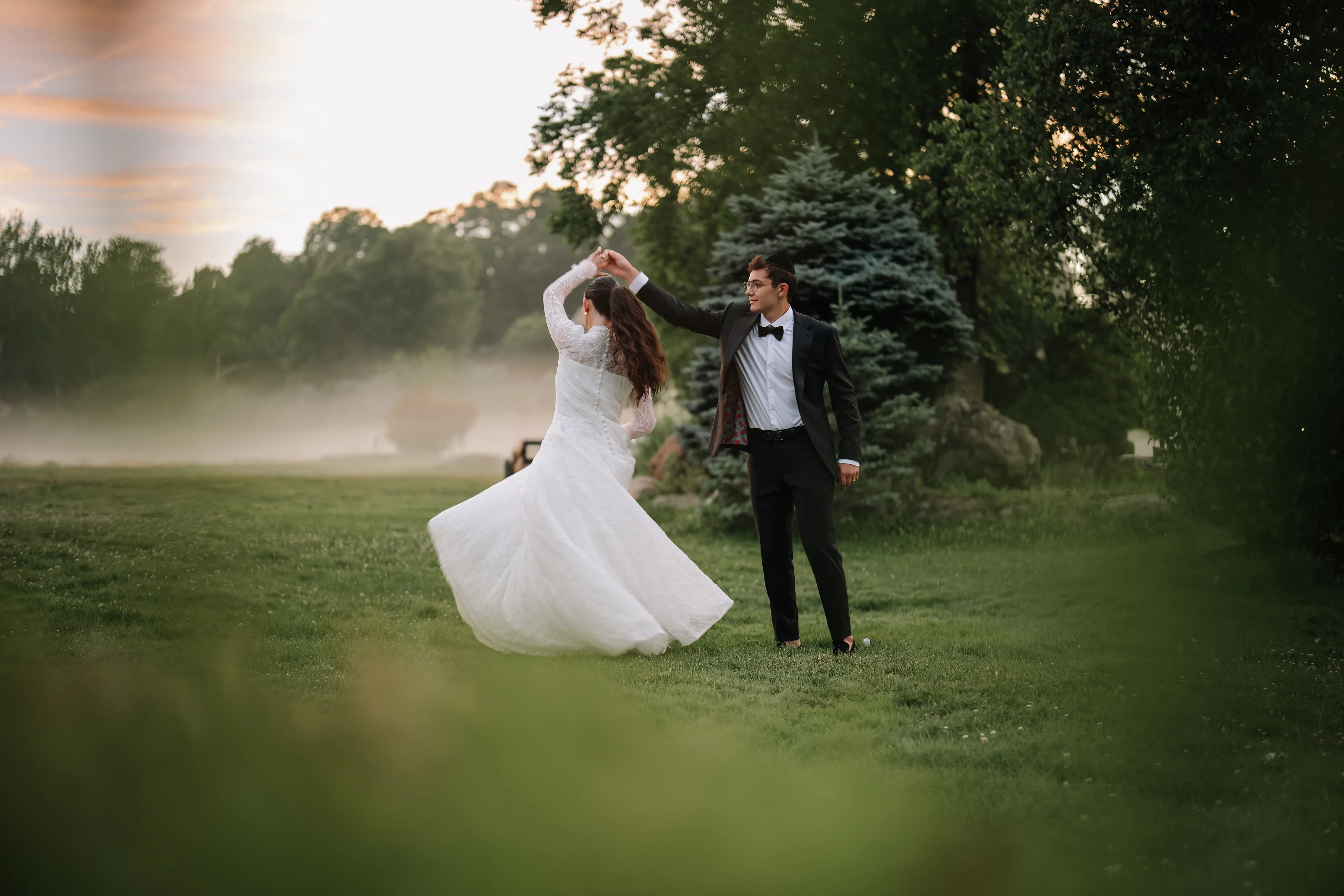 Bride twirling in a flowing wedding gown with groom in formal attire during golden-hour outdoor portraits.