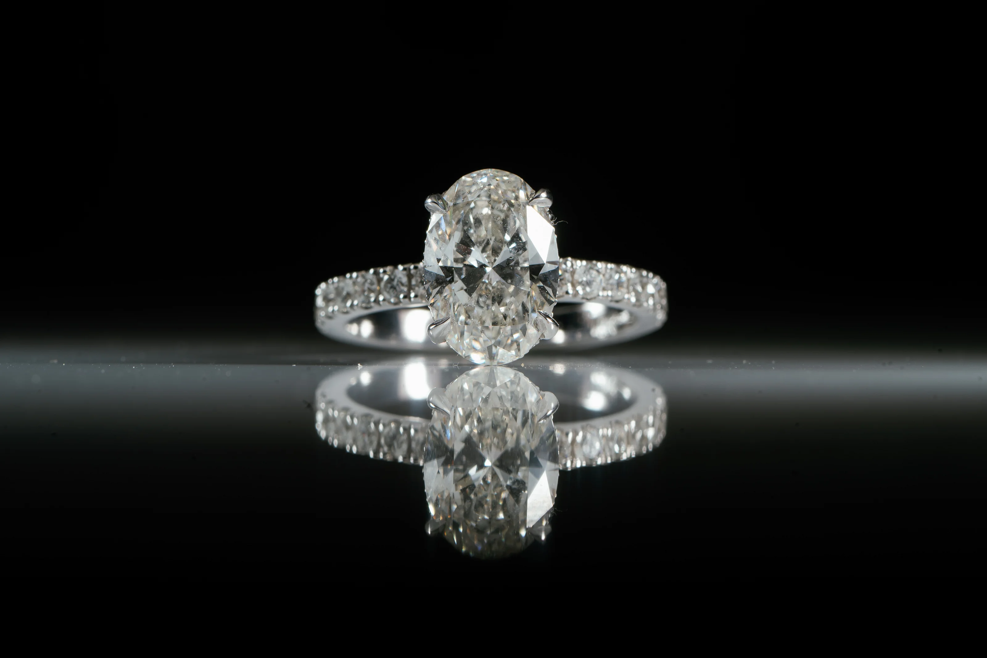 Macro studio photo of a diamond engagement ring centered on a reflective surface with a black background.
