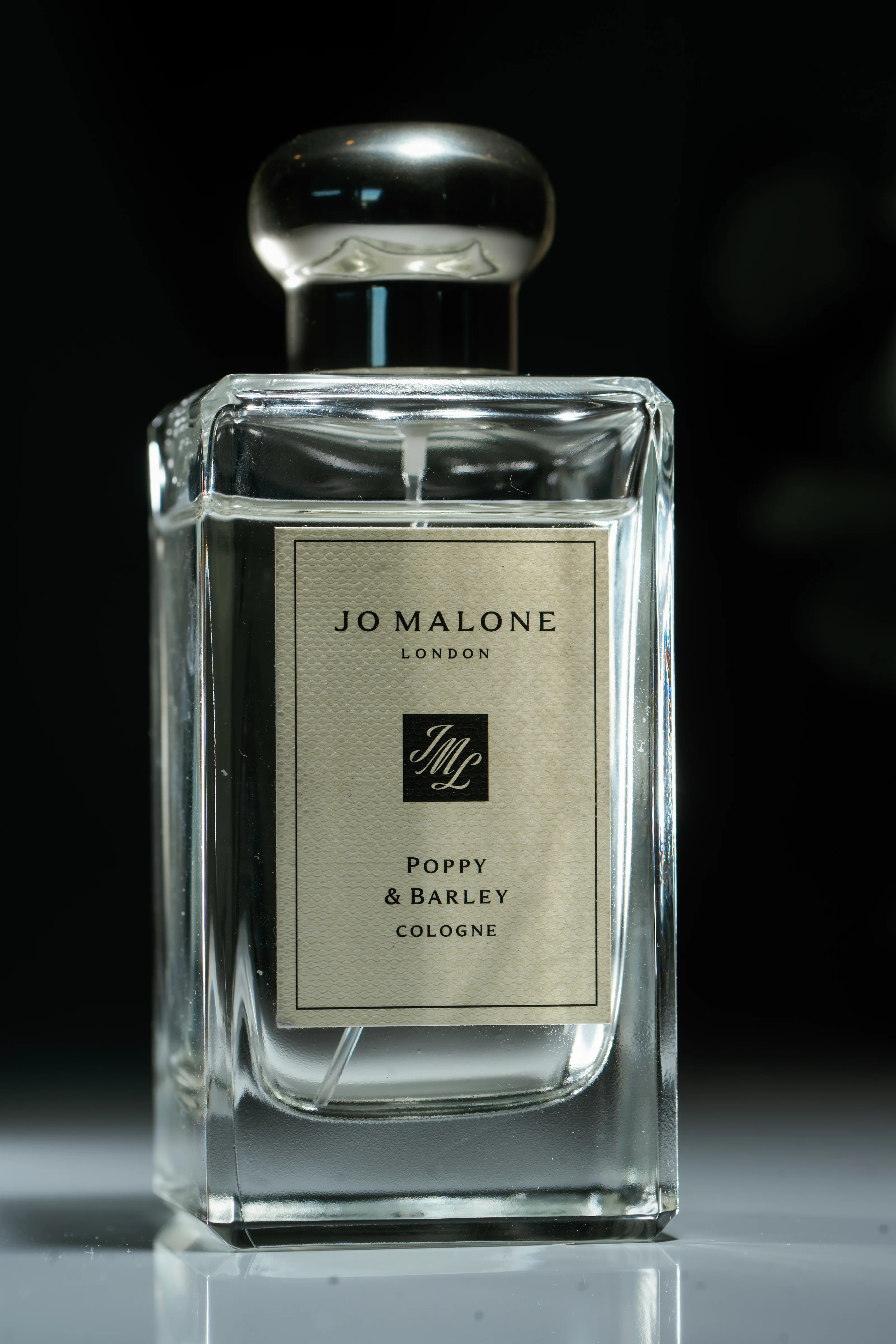 Close-up of a clear Jo Malone London fragrance bottle on a reflective surface with a visible label.