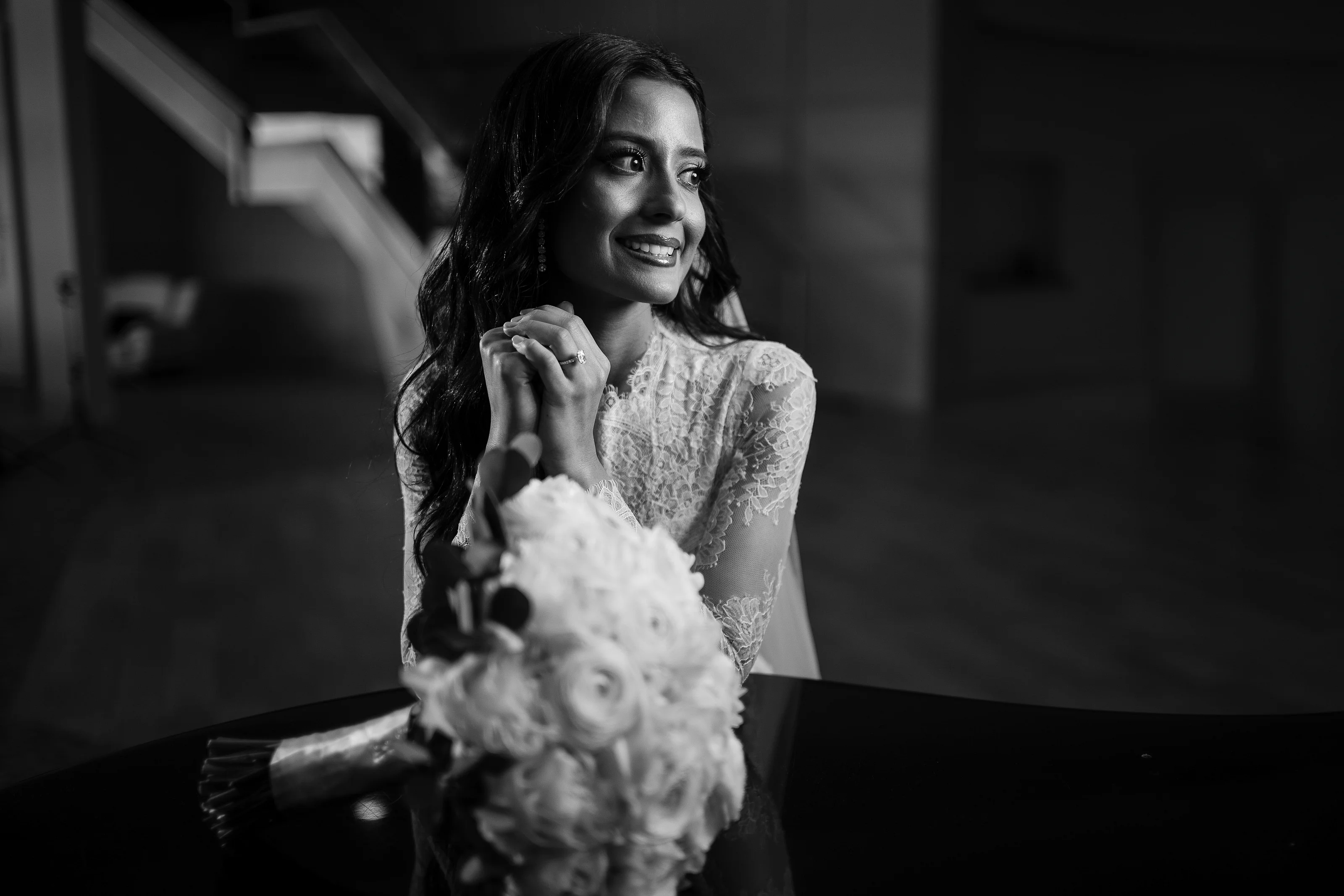 Black-and-white portrait of a smiling bride in lace sleeves with a soft, dramatic background and reflective foreground.