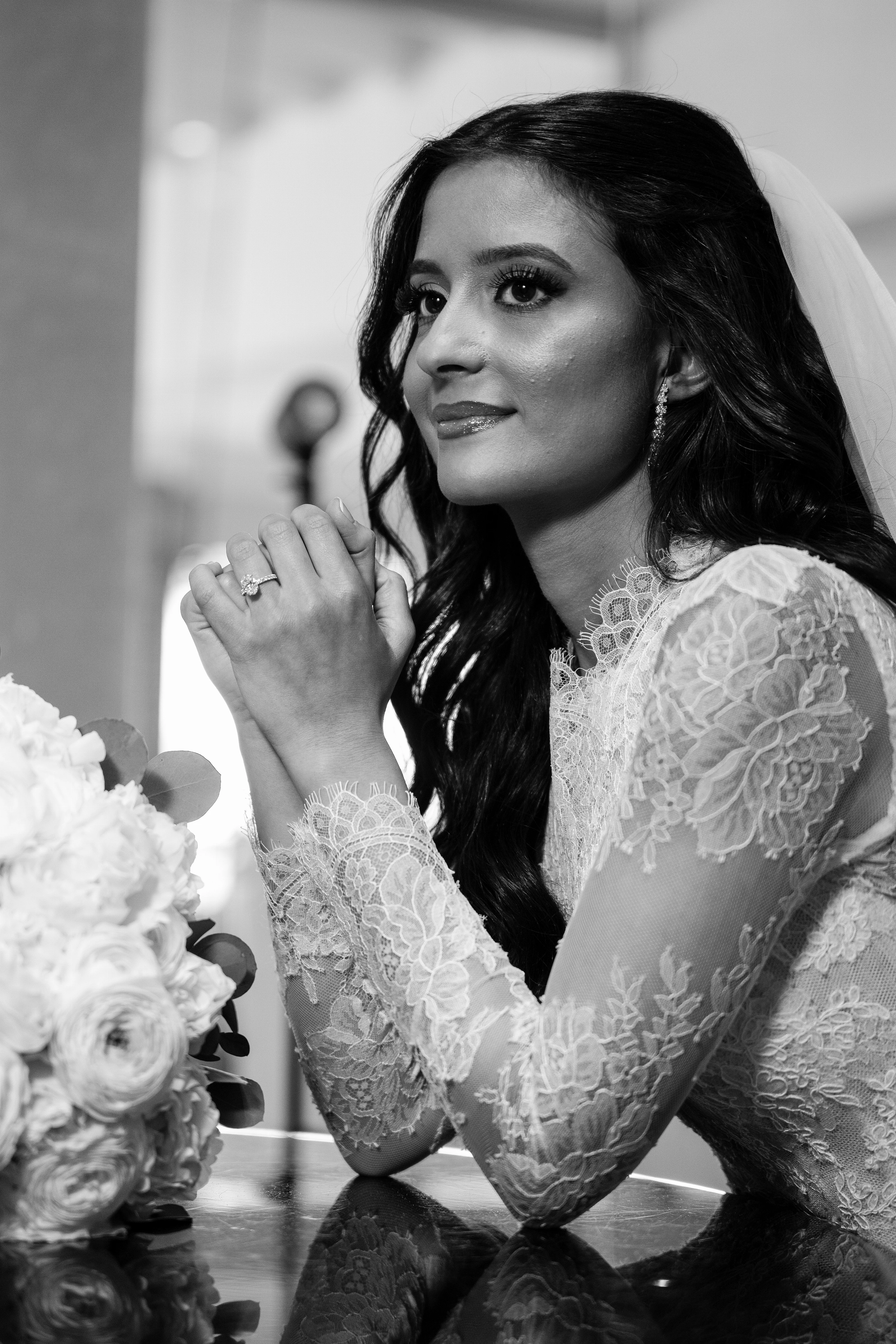 Black-and-white bride portrait with lace sleeves, soft expression, and a bouquet in the foreground.