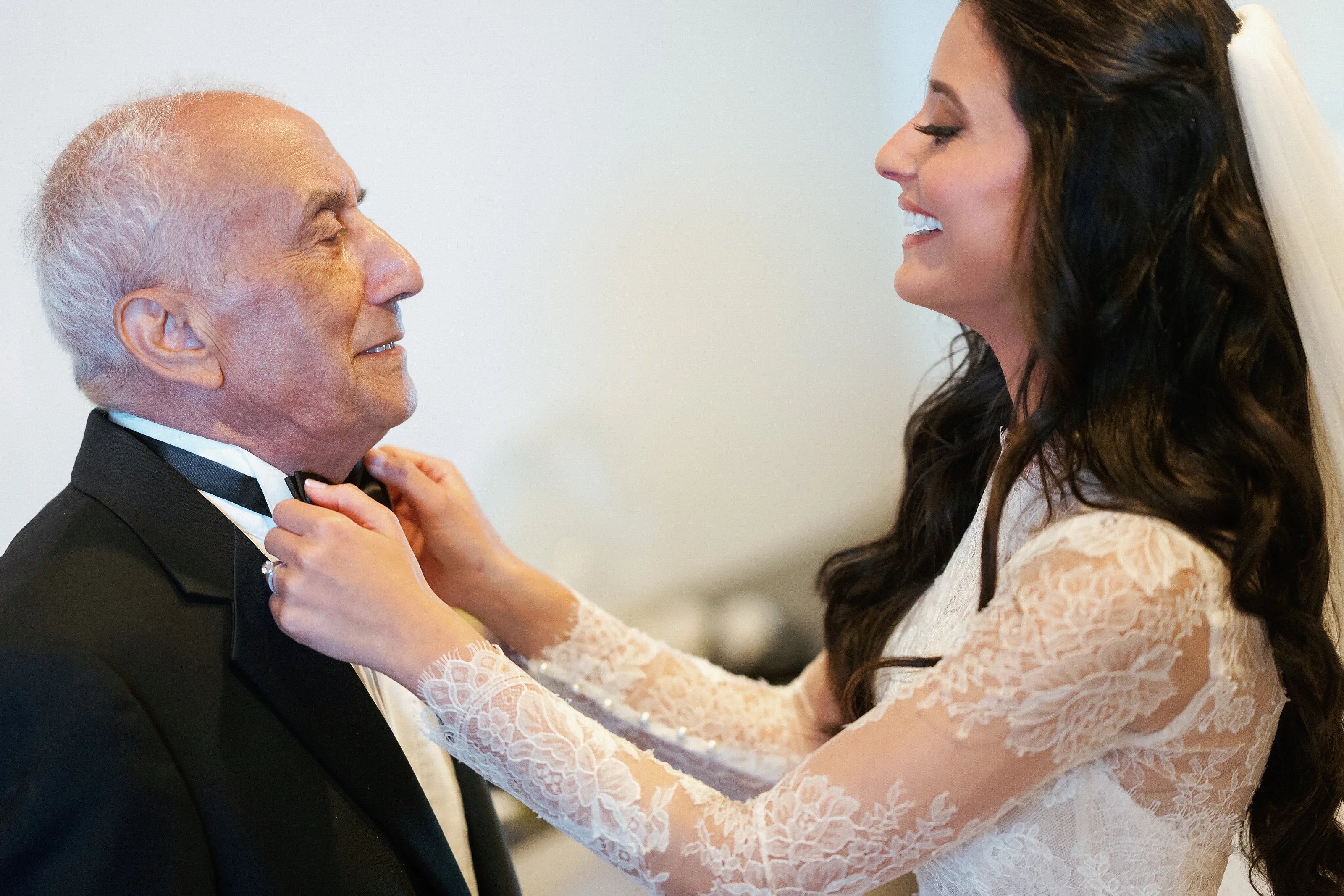 Bride smiling in profile as she adjusts the groom’s collar during a quiet pre-wedding moment, close-up.