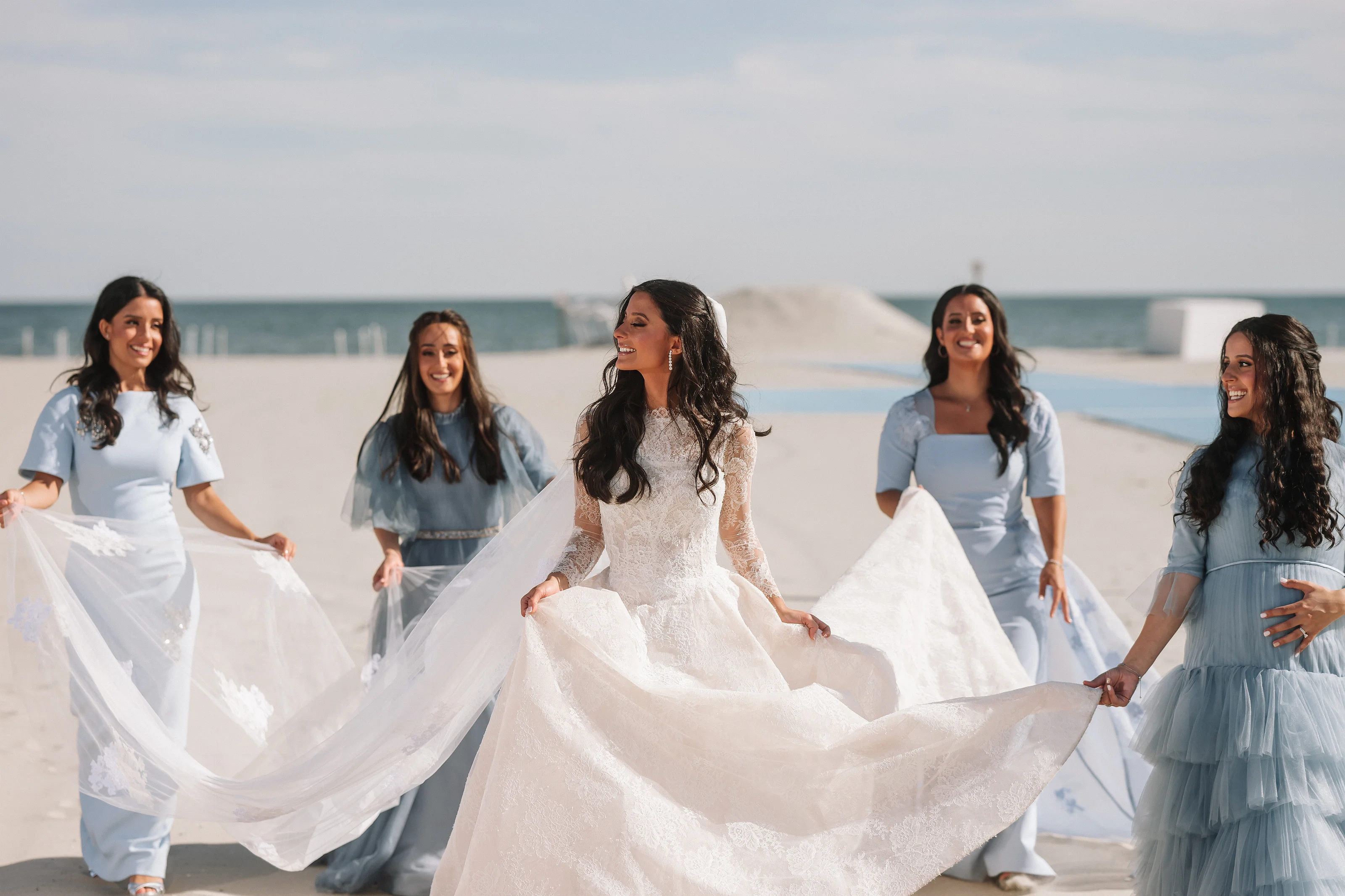 Bride twirls with a flowing skirt while bridesmaids smile and move behind her on a seaside wedding day.