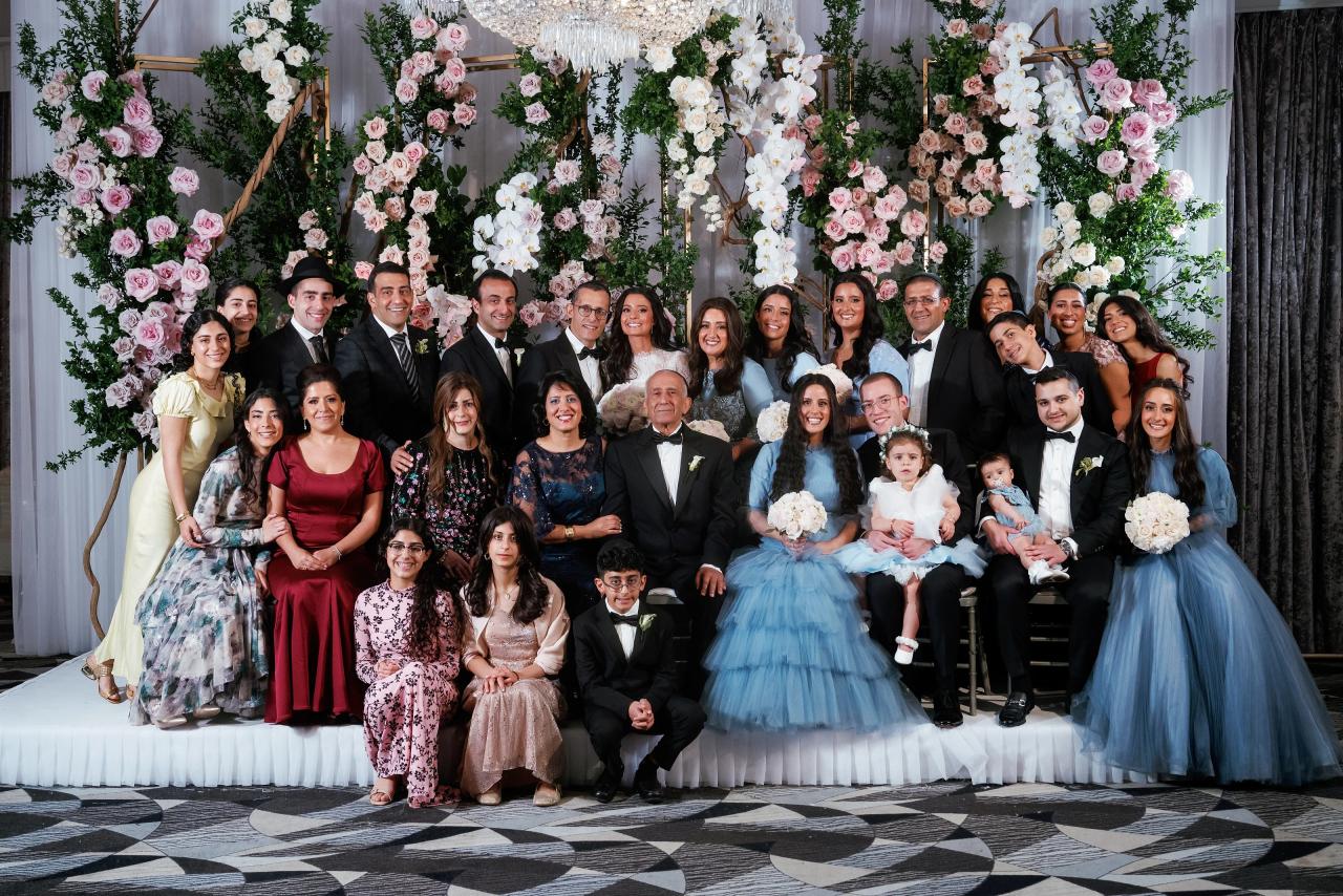 Large group family portrait from a wedding or mitzvah, posed in front of an elaborate floral backdrop with greenery and pastel flowers. Wedding photography at Sands, Atlantic Beach, NY.