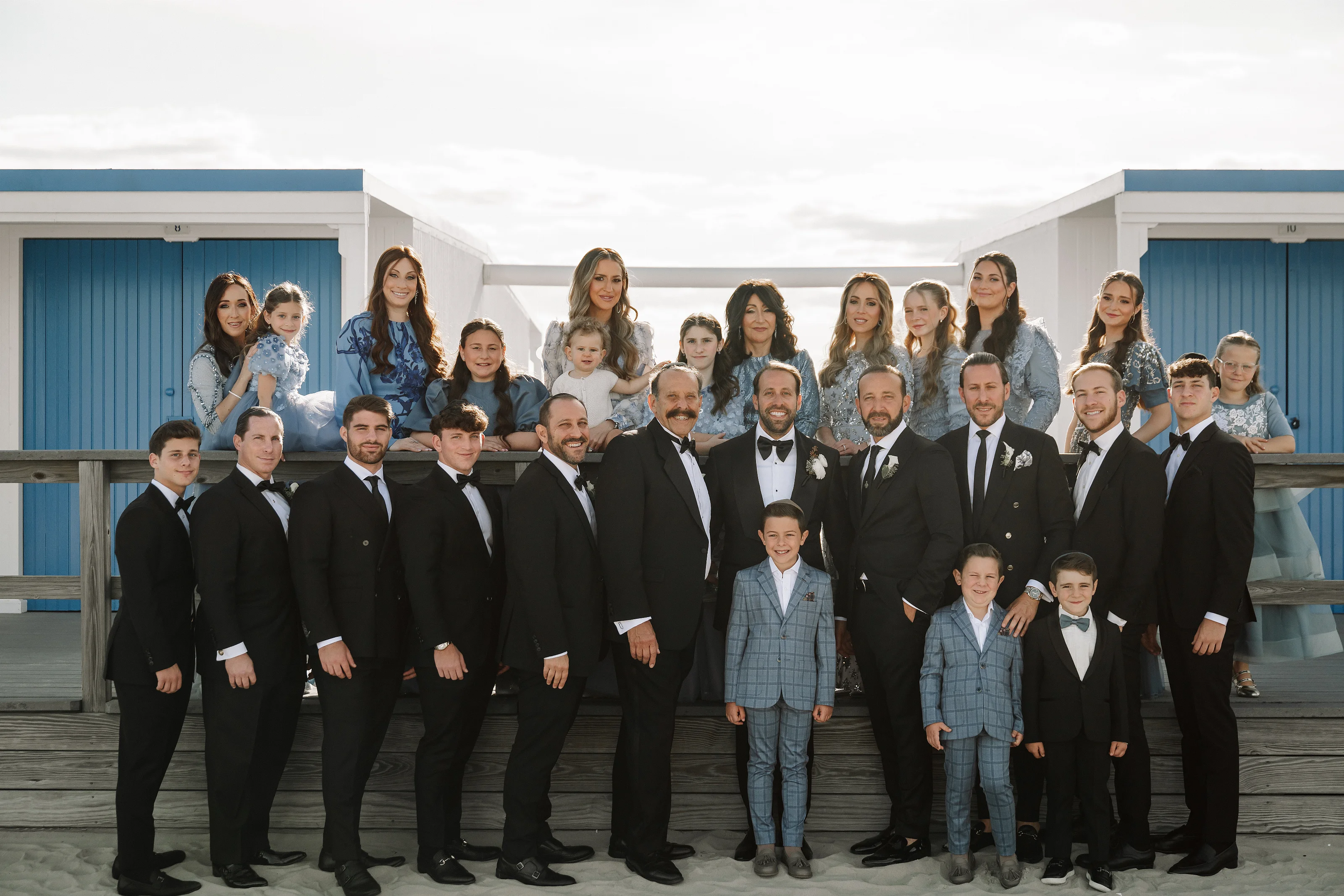 Group family formal portrait with bride and groom in the center, surrounded by family members on a blue-and-white building walkway.