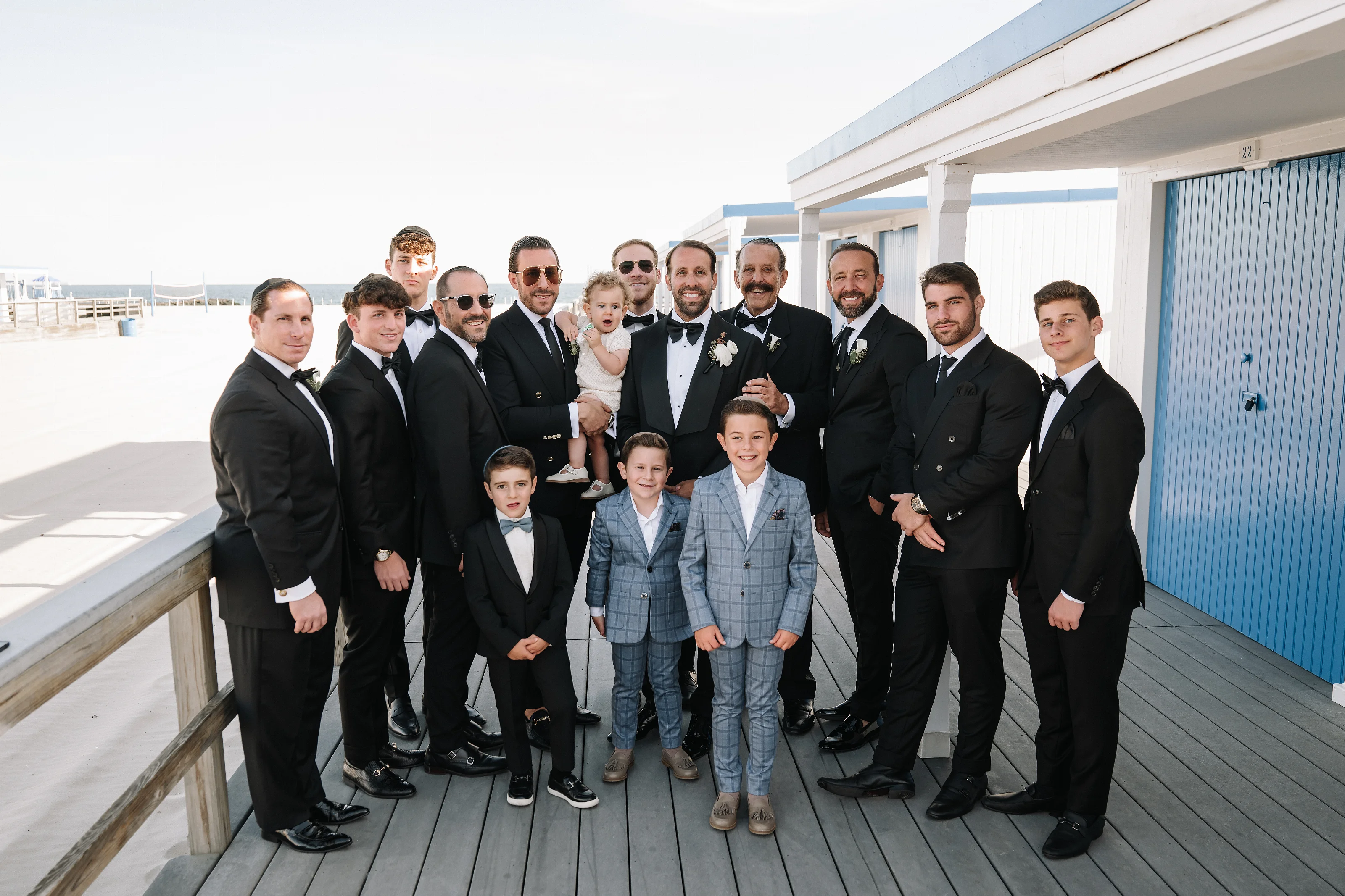Wedding day group formal portrait of the groom and family outdoors under a portico on a wooden boardwalk.
