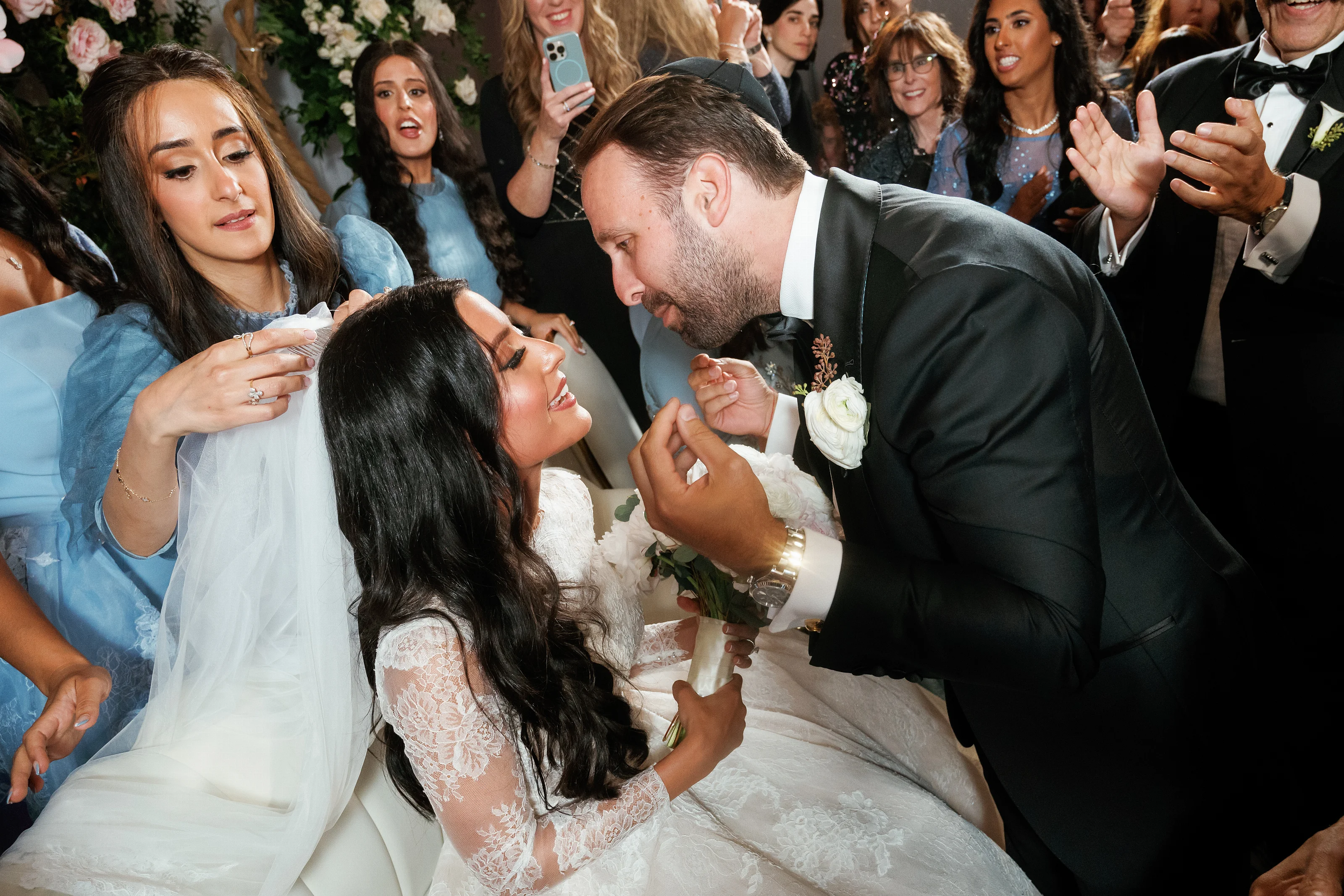 Bride and groom leaning in and laughing while guests in formal attire watch and cheer in the background.