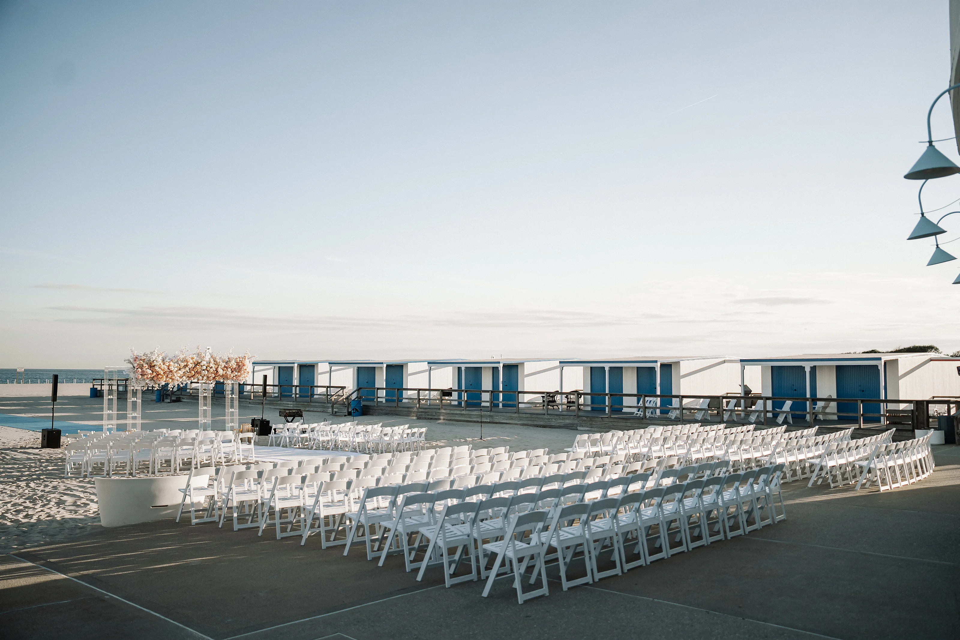 Row of white wedding ceremony chairs facing the front outdoors by the water under a bright sky.