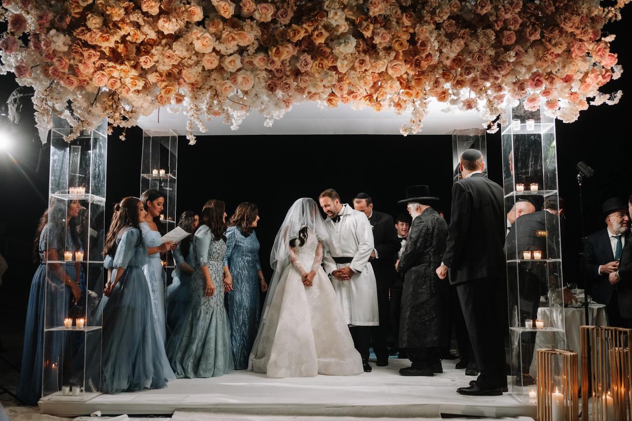 Bride and groom sharing an intimate badeken moment under a floral canopy and candlelit chuppah, with guests gathered at the sides. Wedding photography at Sands, Atlantic Beach, NY.