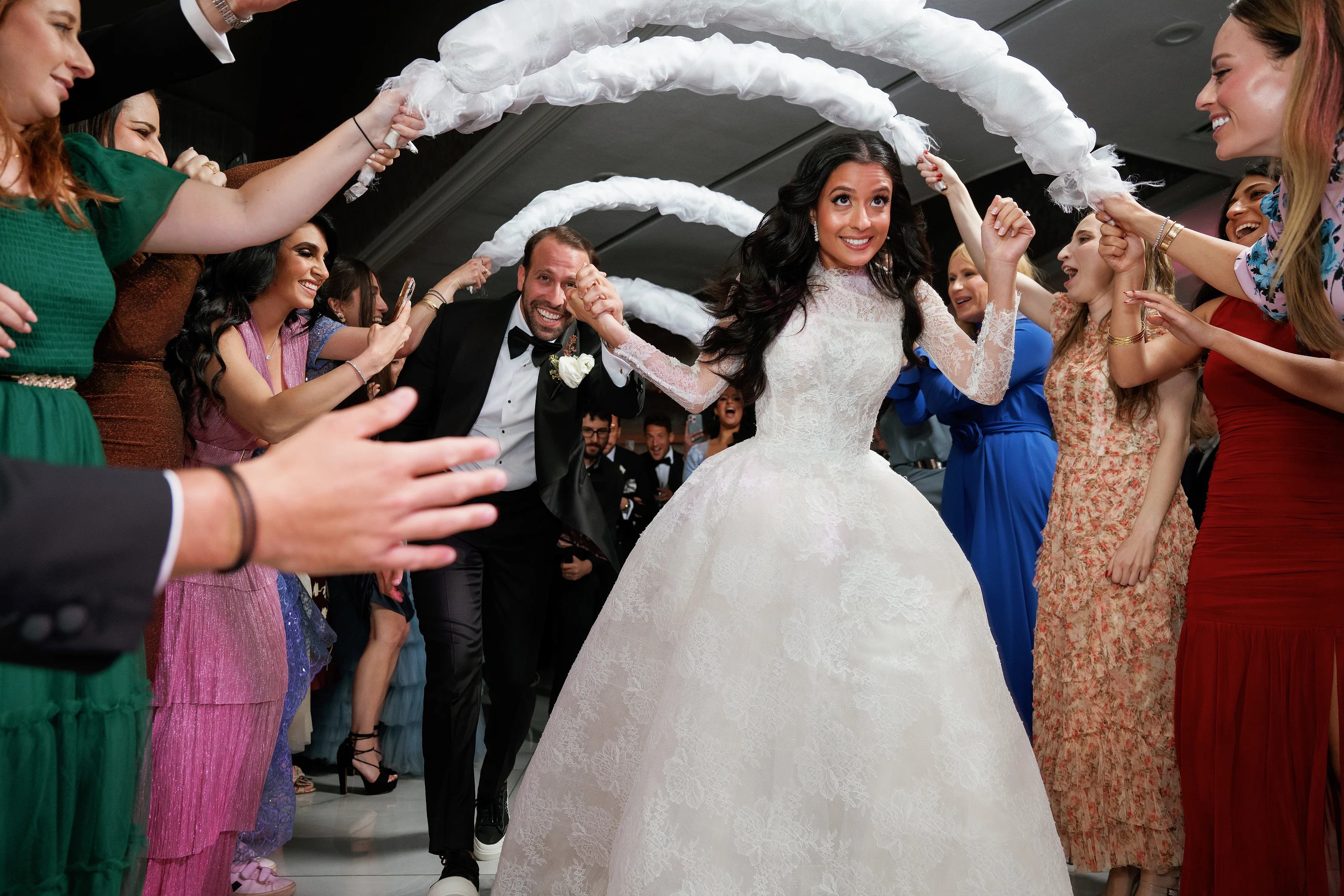 Bride being lifted during wedding celebration with friends cheering and reaching in under a fabric arch.