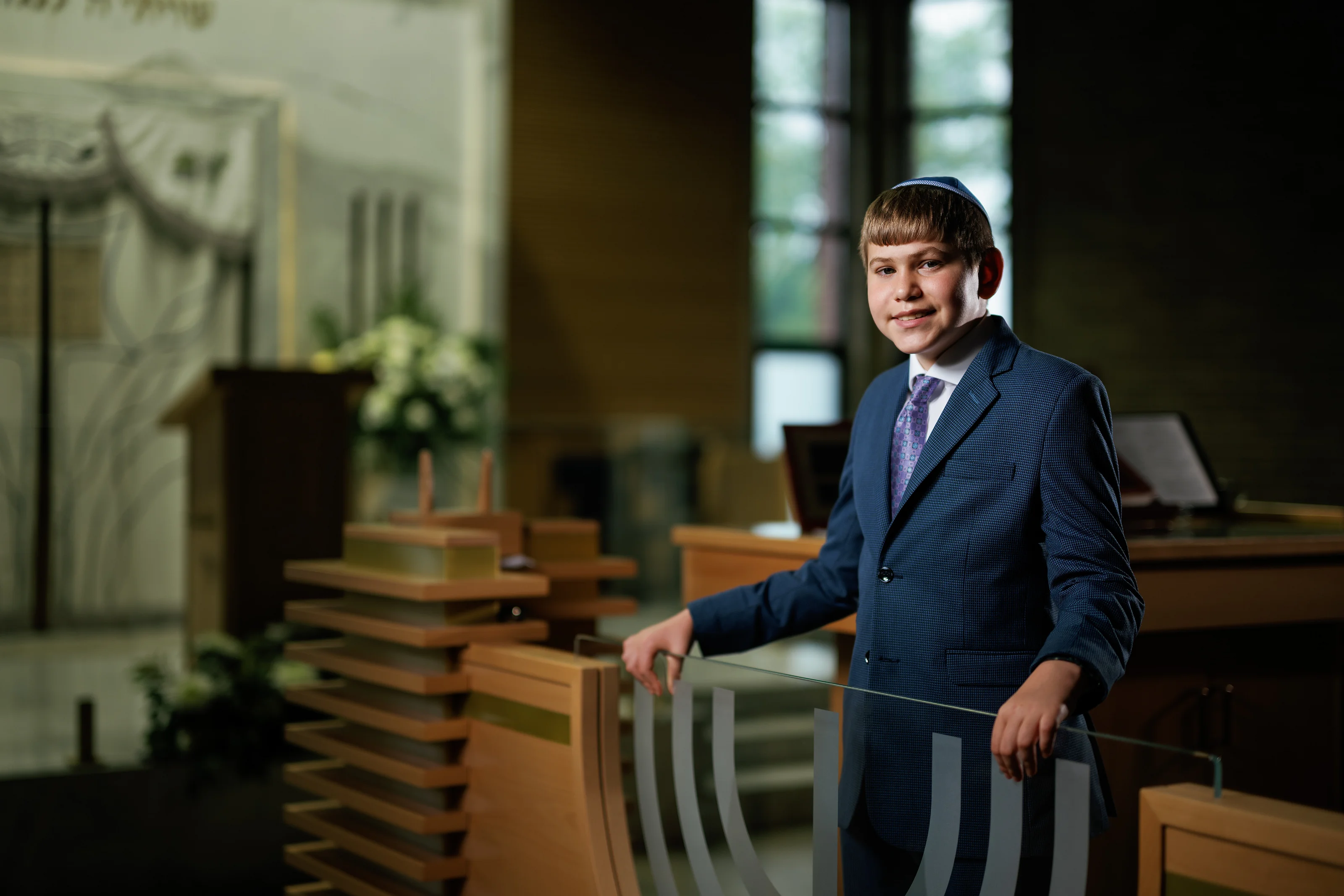 Boy in a suit standing by a railing inside a sanctuary with soft background blur and side window light.