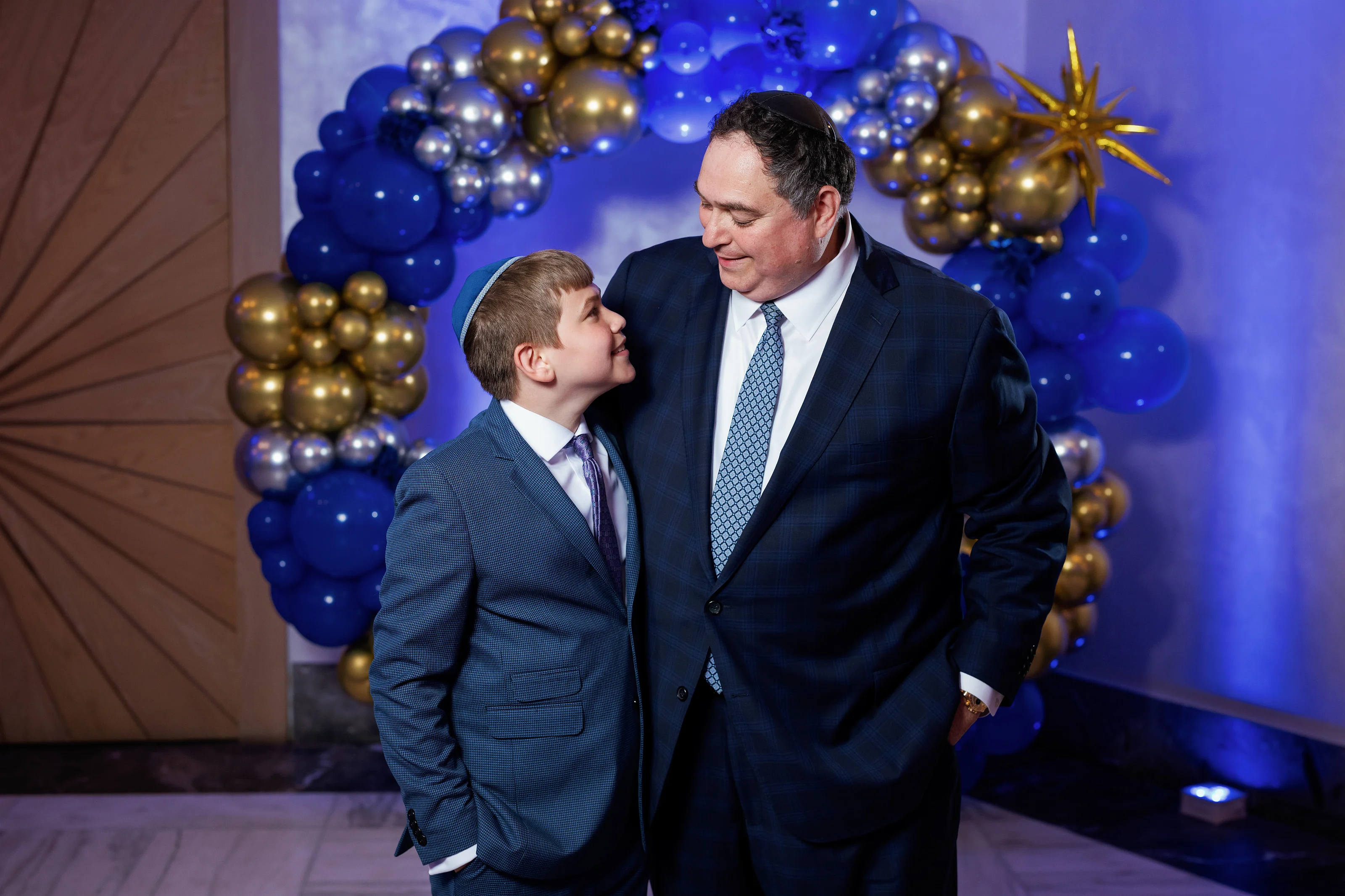 Father holding his young son close during a blue-and-gold celebration, both smiling with affectionate eye contact.