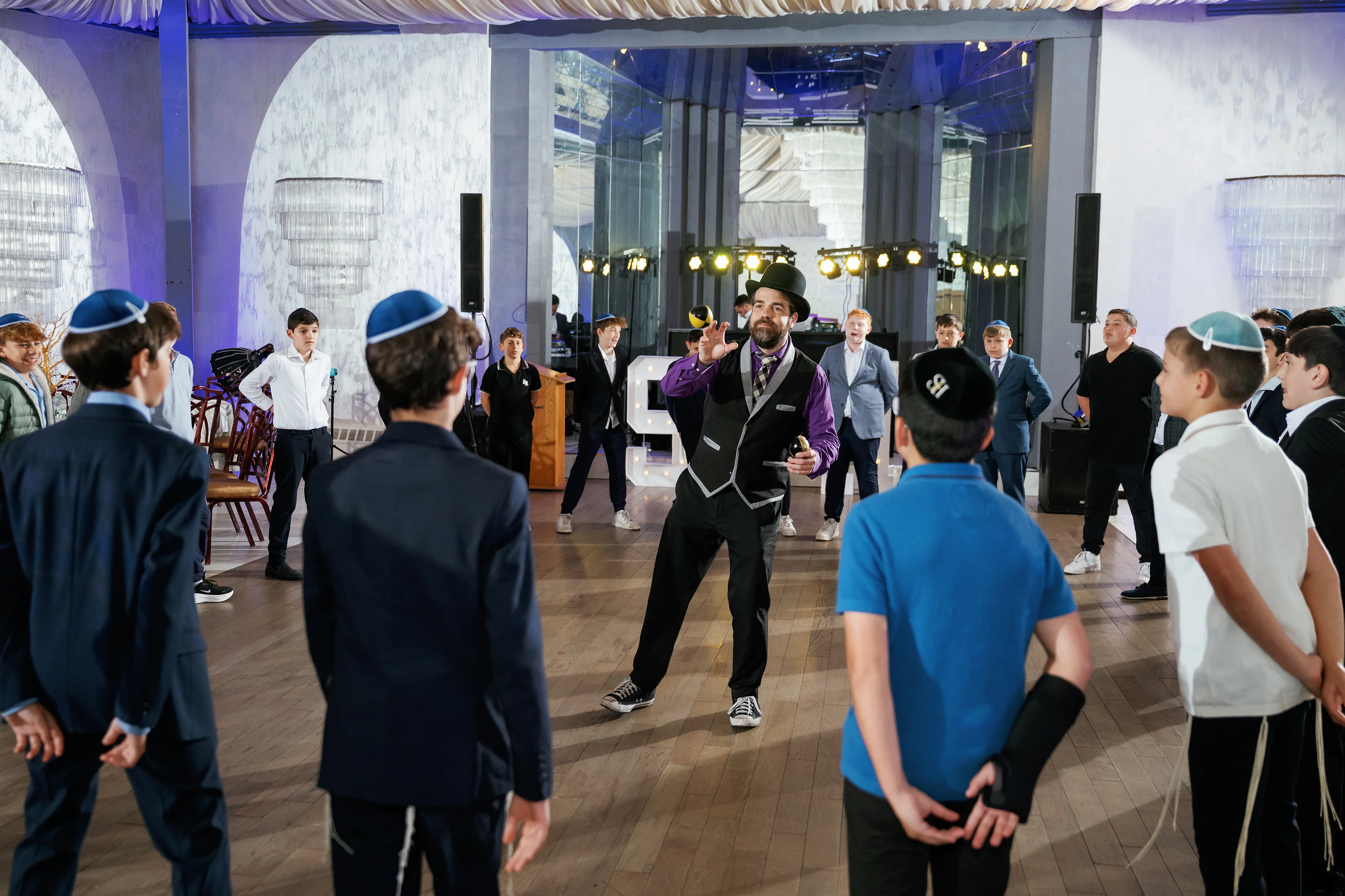 Guests gathered in a lit event hall watching a man gesture on the dance floor during a celebration.