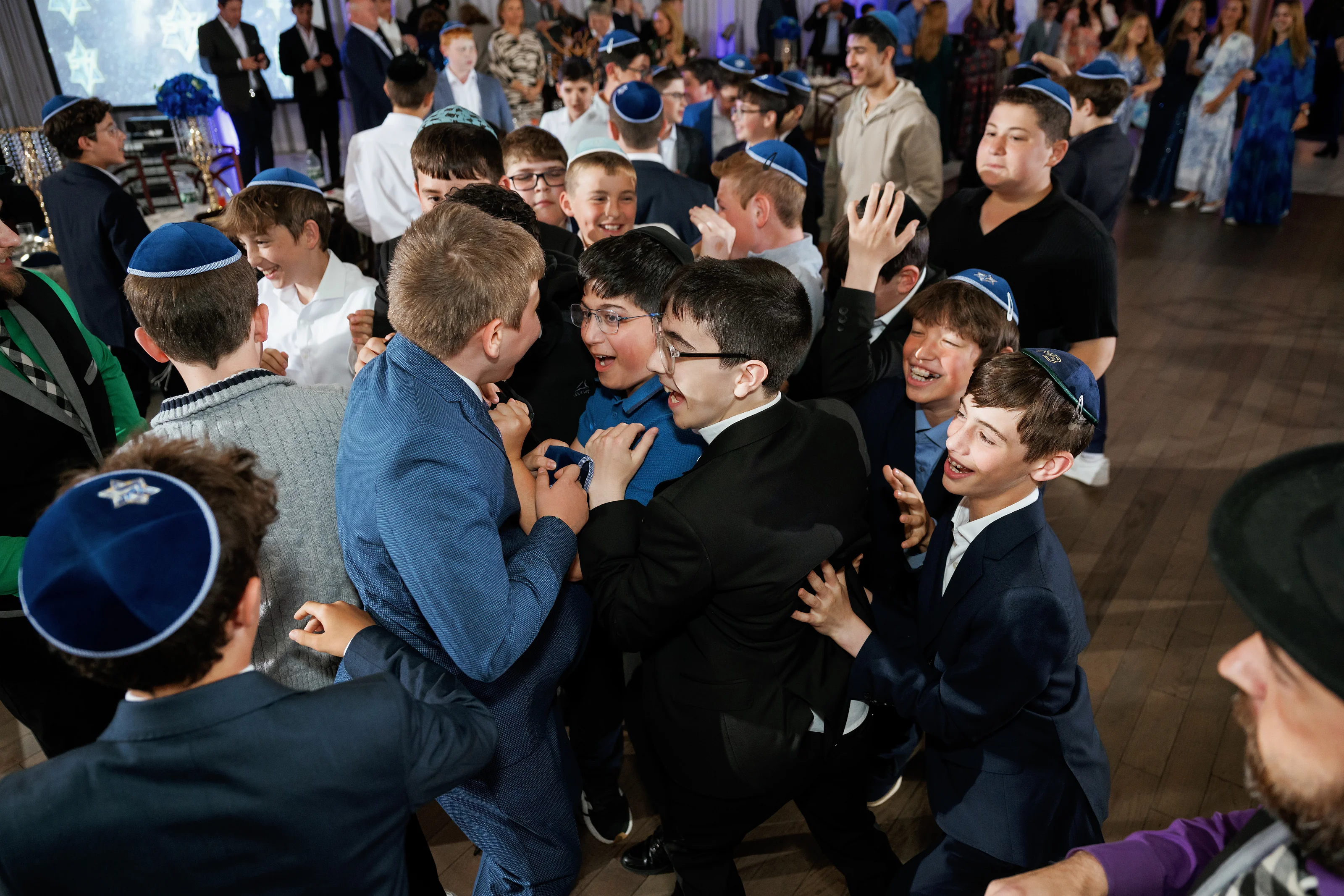 Smiling children in formalwear wearing blue head coverings cheer and laugh together during a lively celebration.