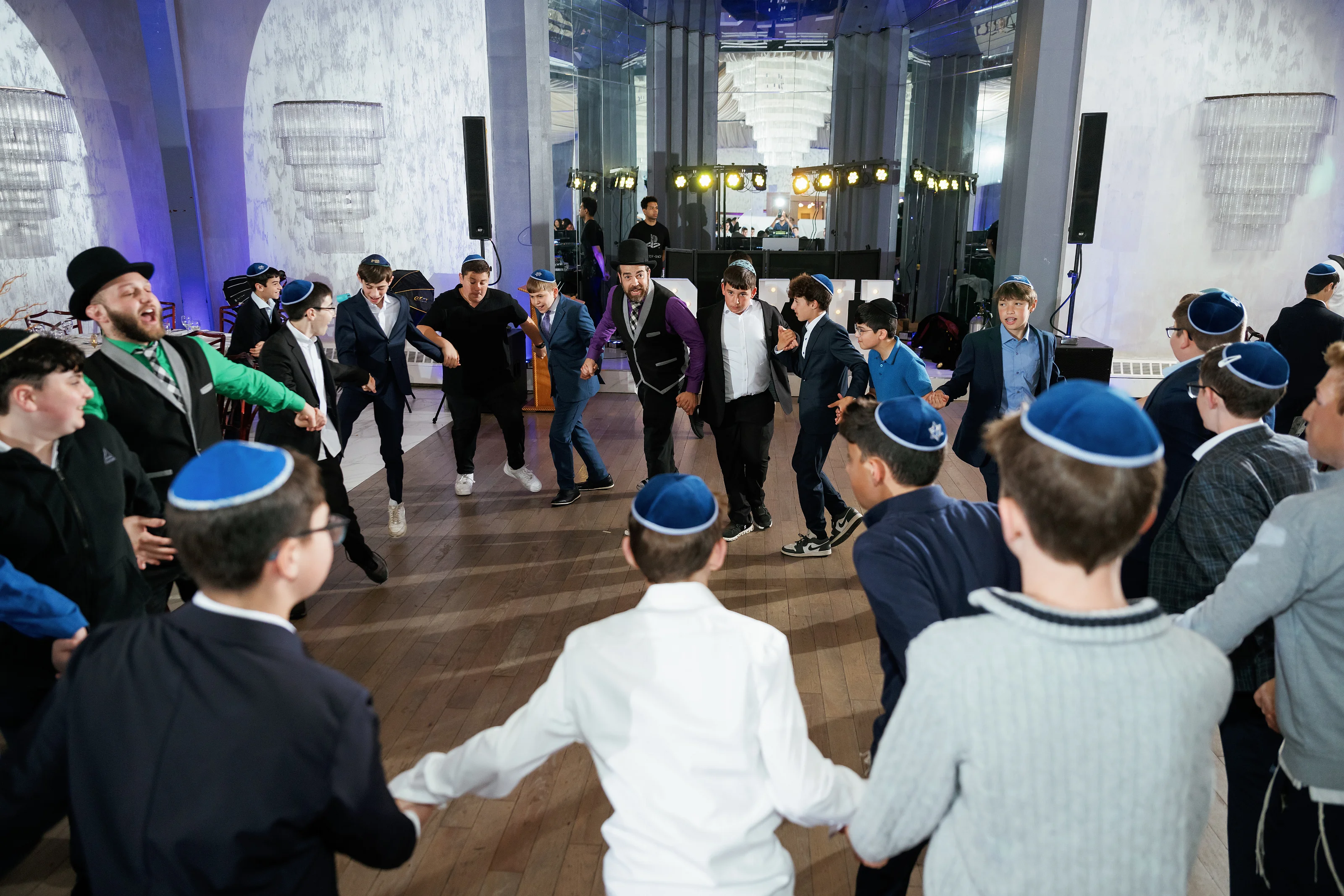 Guests dancing together indoors at a wedding, captured in motion under blue lighting and architectural beams.