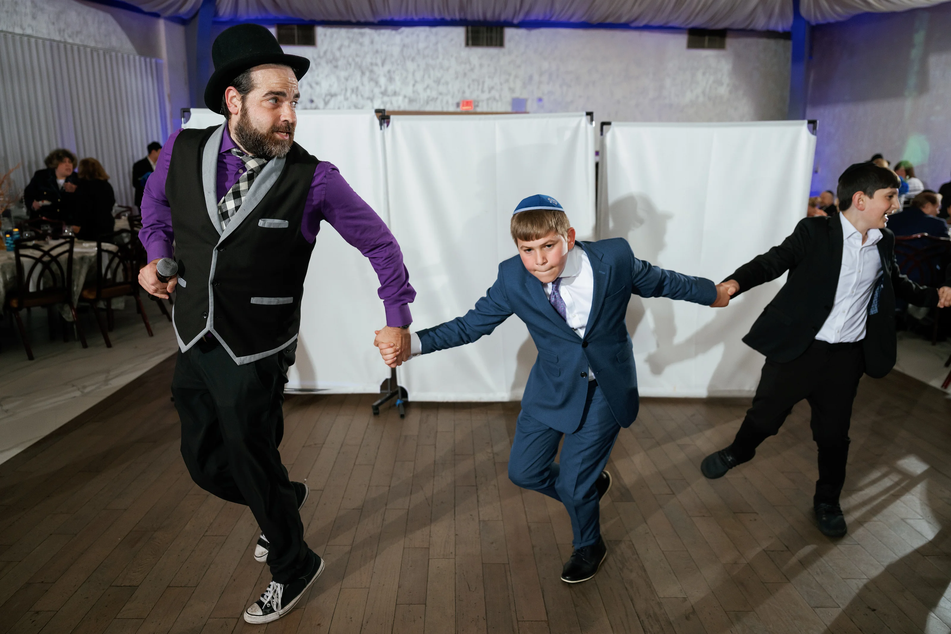 Candid dance-floor moment at a celebration with three men in formal attire moving in sync under blue accent lighting.