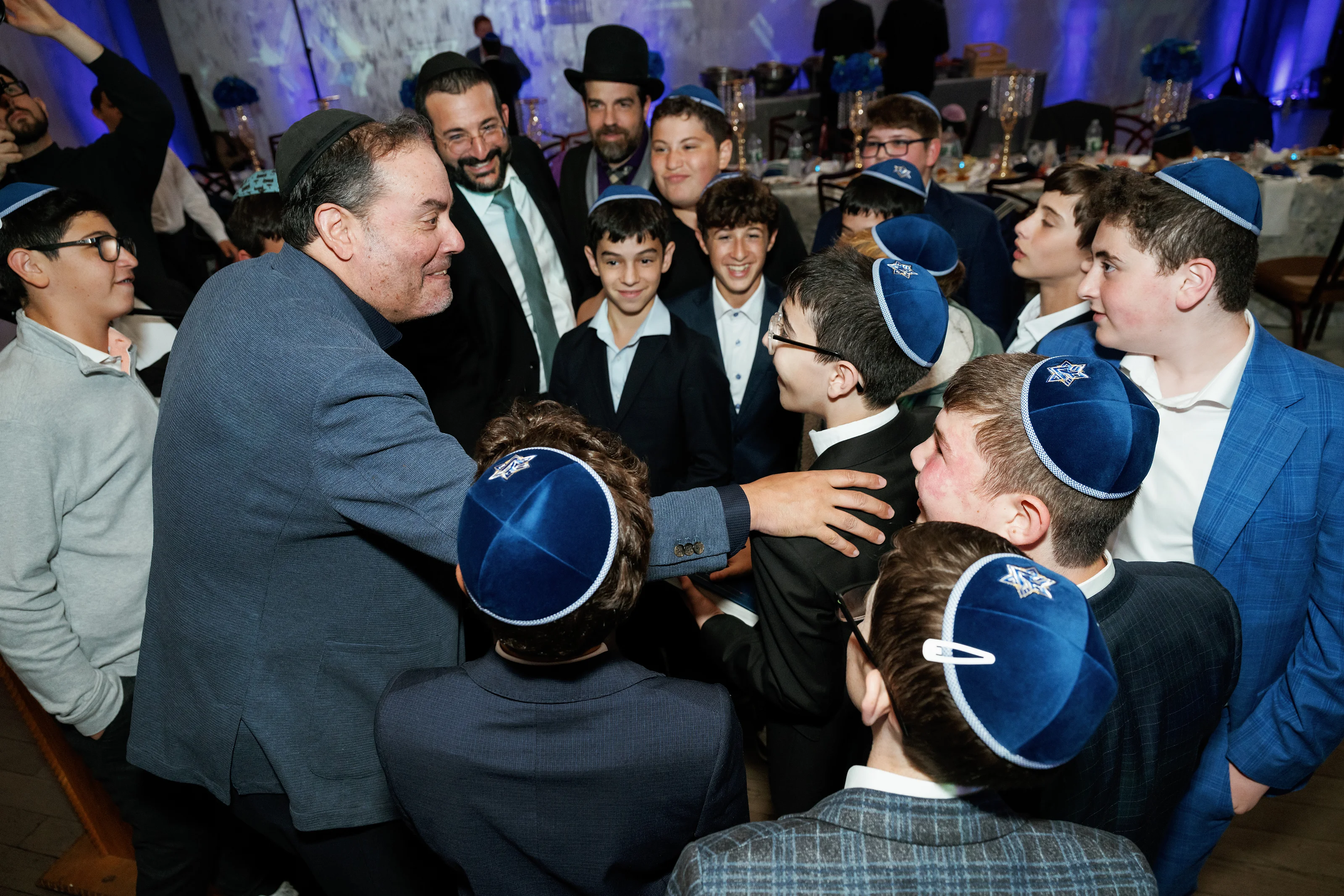 Joyful close-up of guests in blue hats embracing and smiling during a lively celebration under blue event lighting.