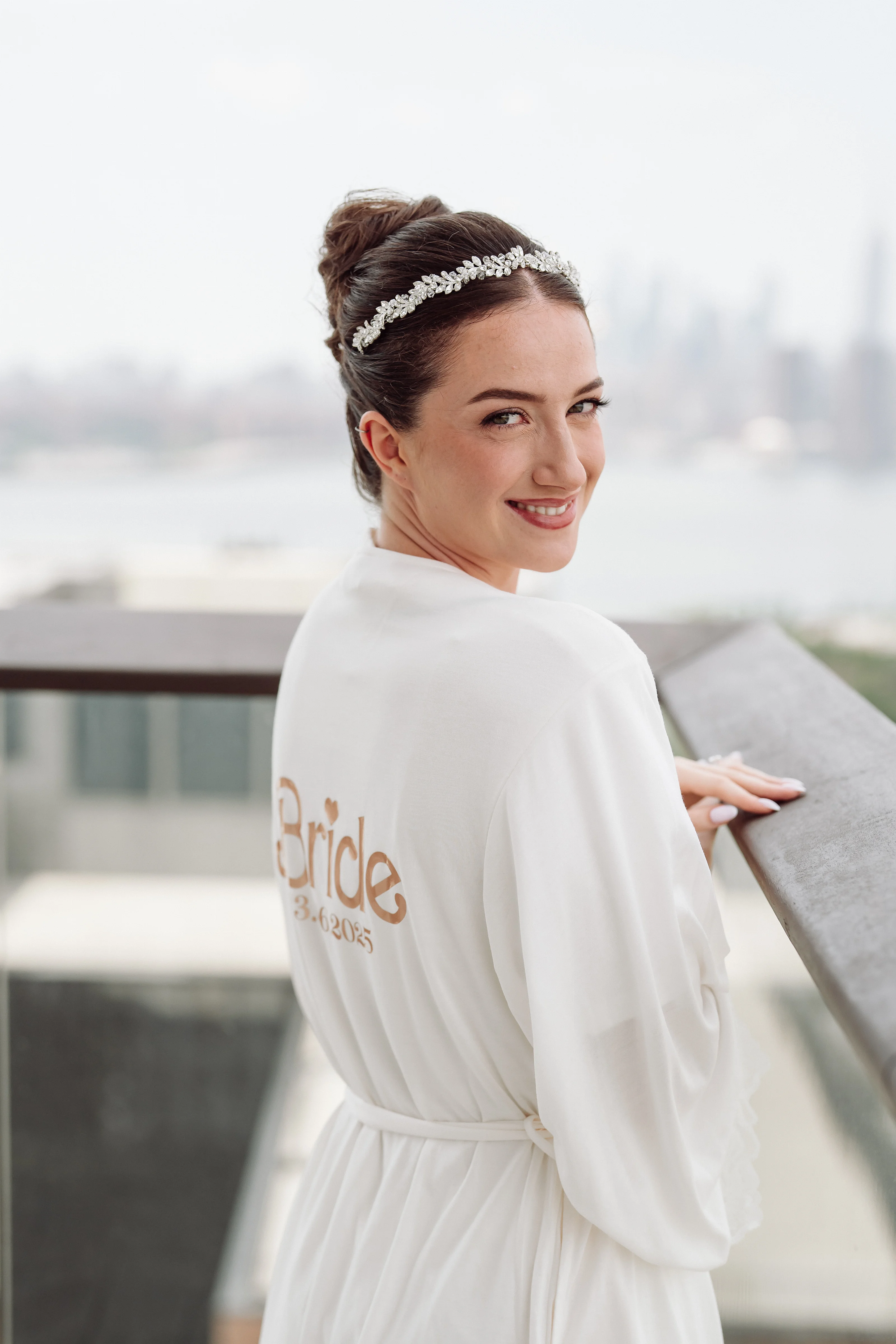 Bride in a white dress and headpiece smiling outdoors with a soft, minimal background.
