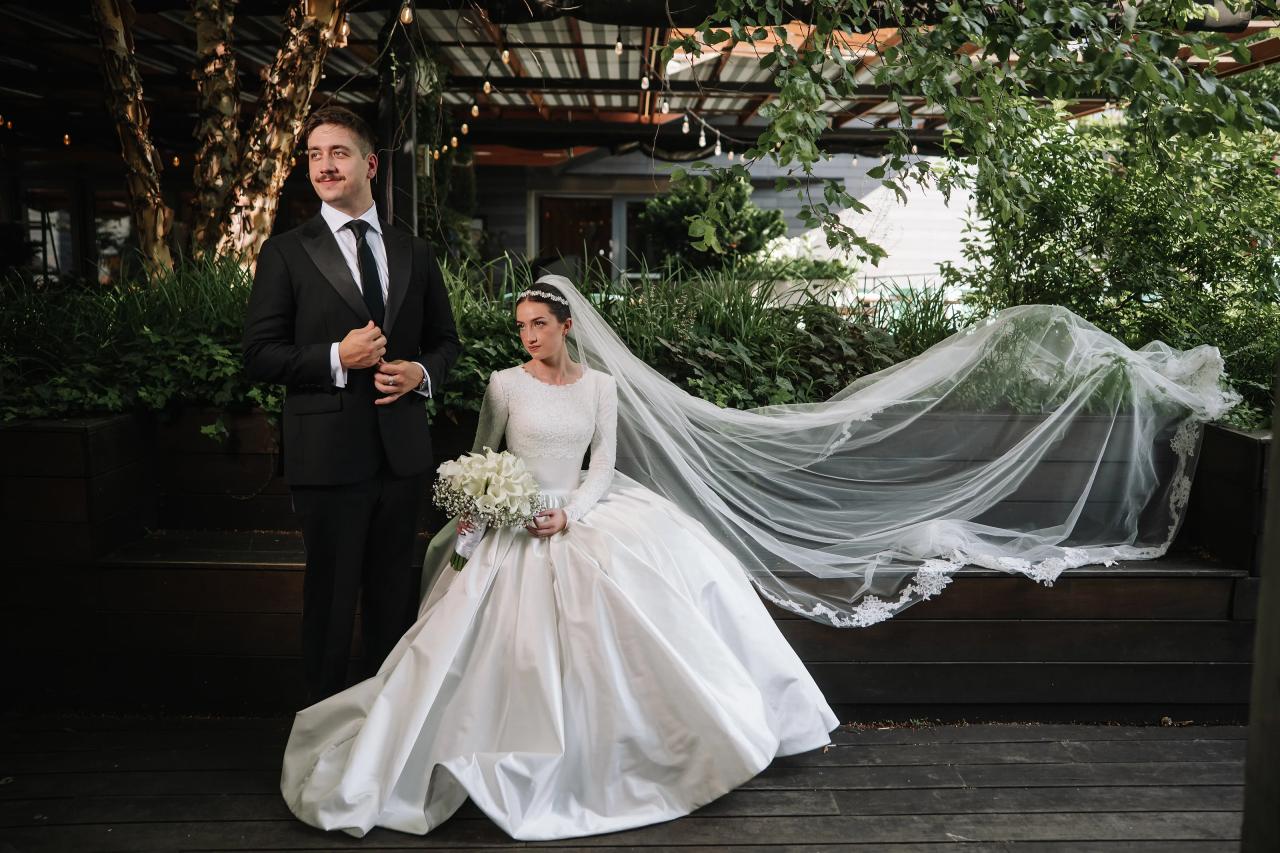 A bride and groom stand together during a wedding moment, with the bride’s veil flowing and greenery surrounding them. Wedding at Ateres Chynka, Brooklyn, NY.
